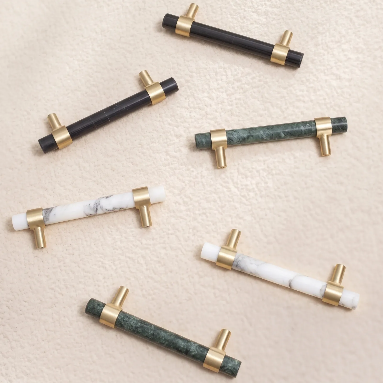 Overhead view of white, green and black marble cabinet pulls with brass collar rings on a pale textured surface.