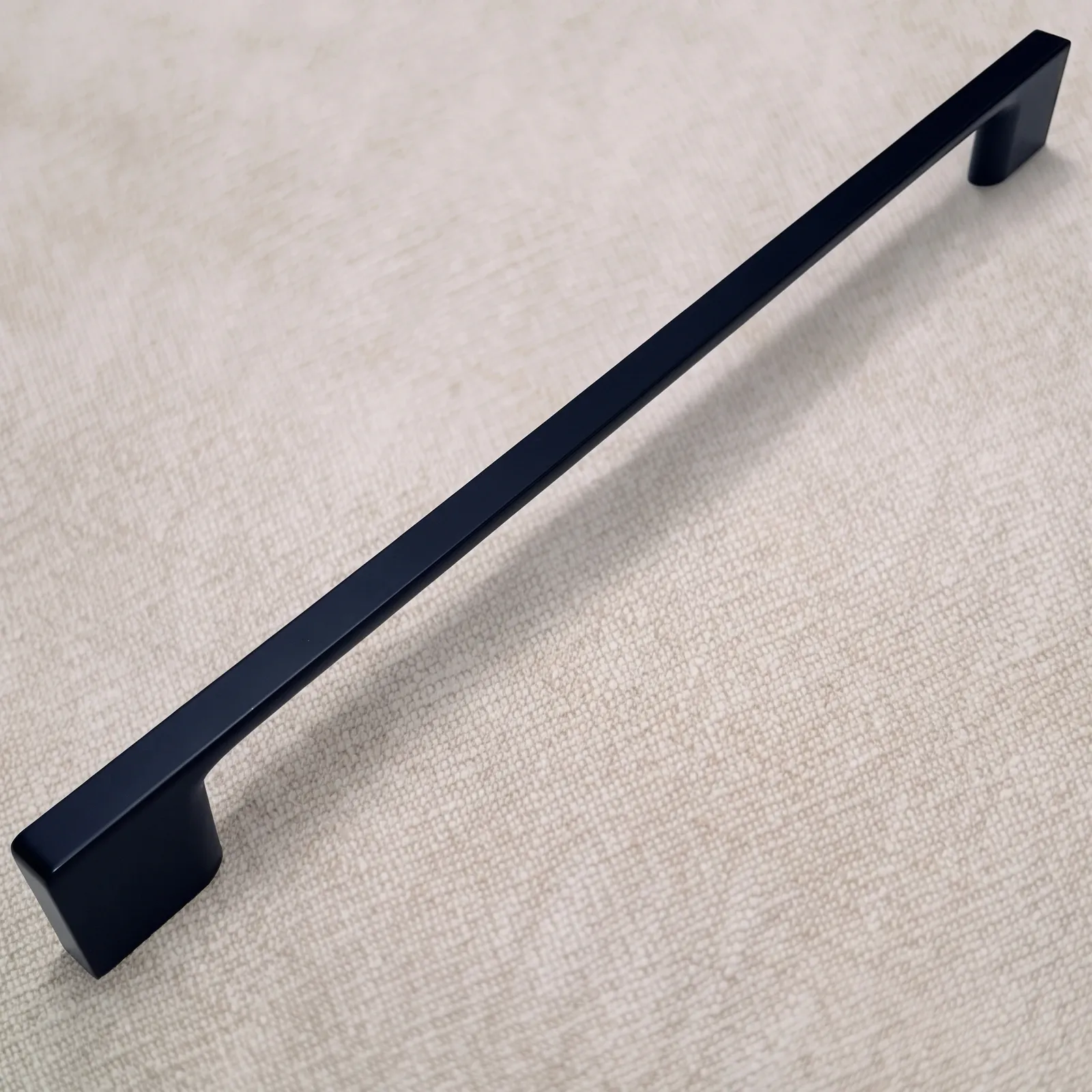 Angled view of a Matt Black D-profile zinc alloy bar pull with a straight flat bar and flared feet on natural linen