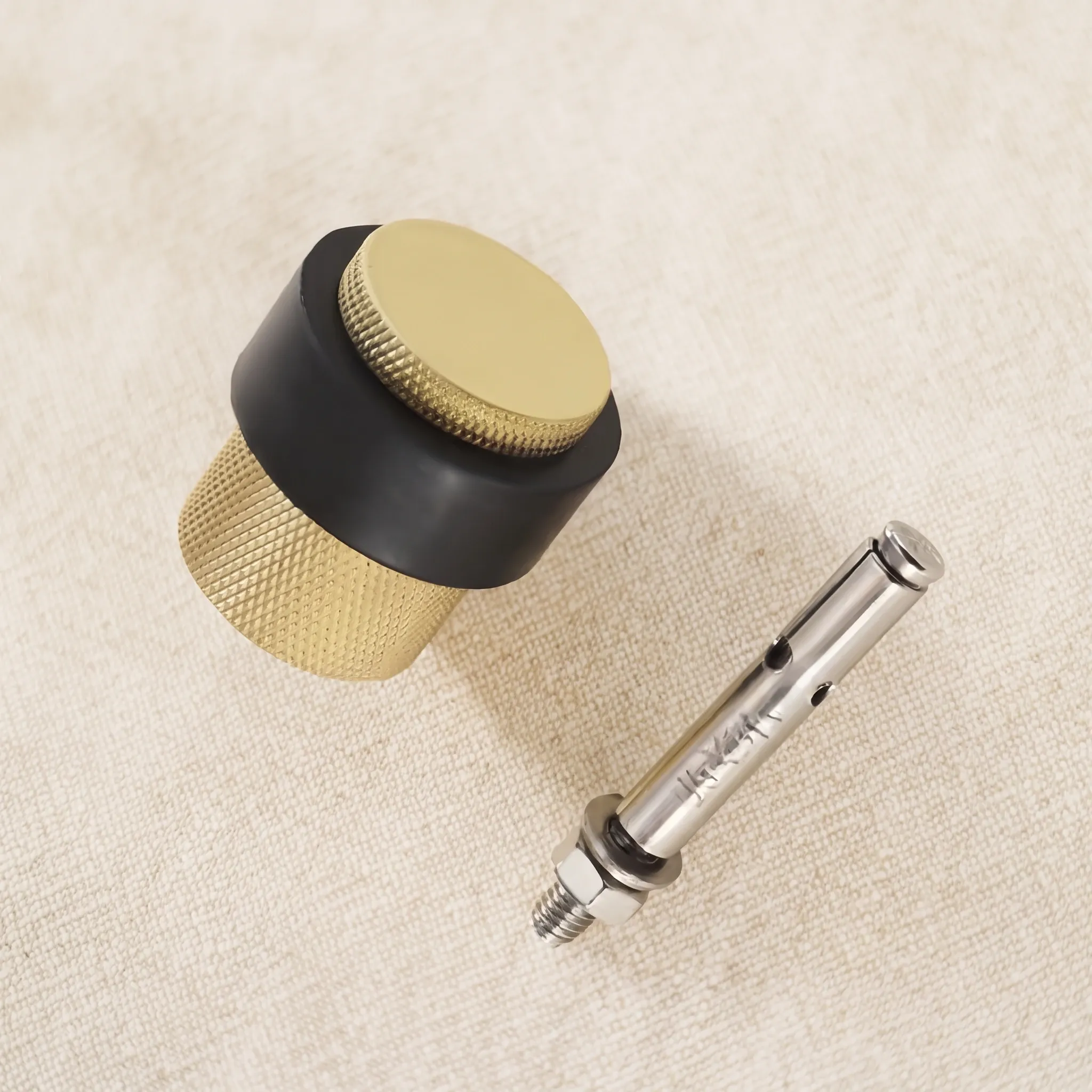 The Brass Gold knurled door stop photographed at an angle with the supplied fixing screw and nut resting beside it.