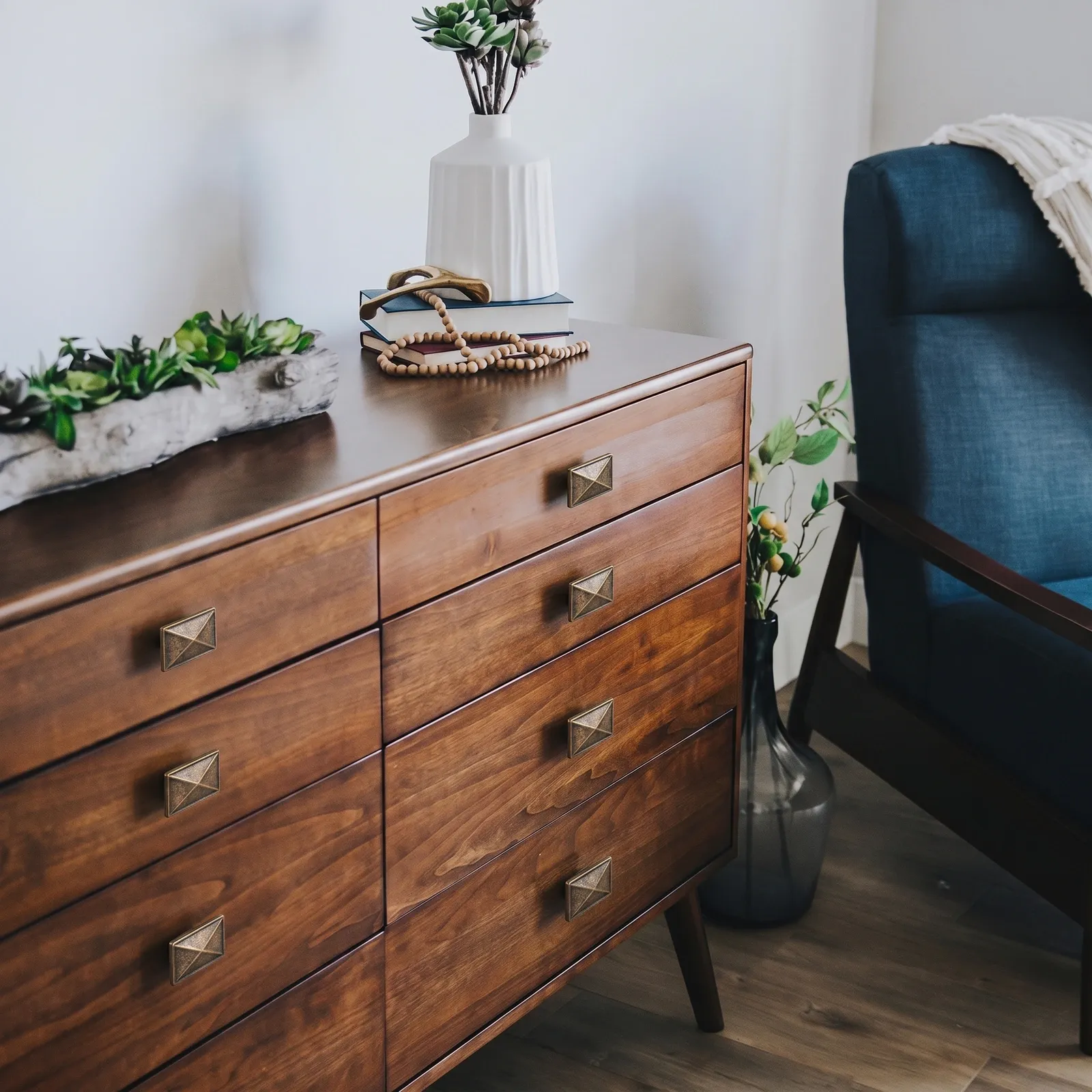 Wooden dresser with antique bronze diamond-face knobs beside a blue armchair in a bright room