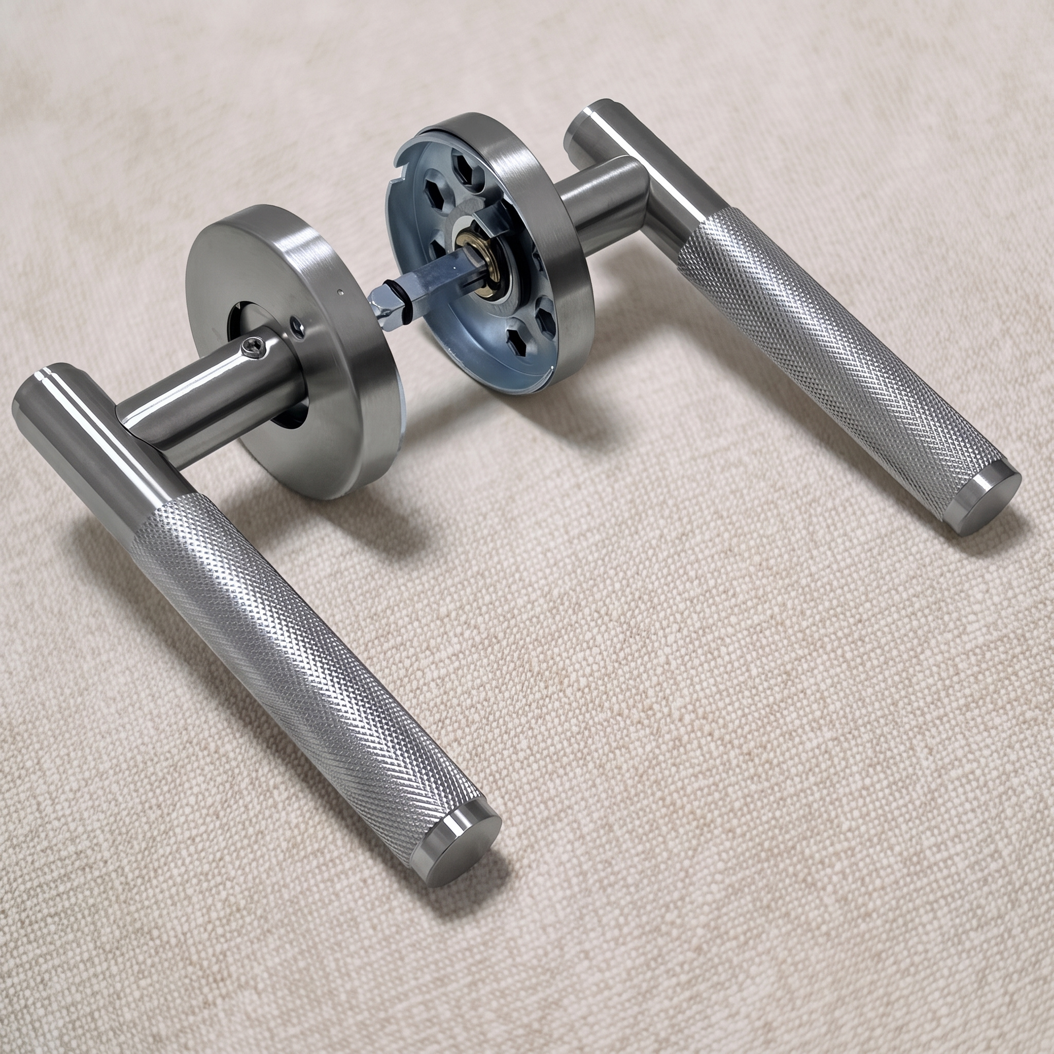 Angled view of a chrome-toned knurled stainless steel lever door handle pair on a warm beige fabric surface, with both round roses and the through-door cassette carrying the square spindle in view