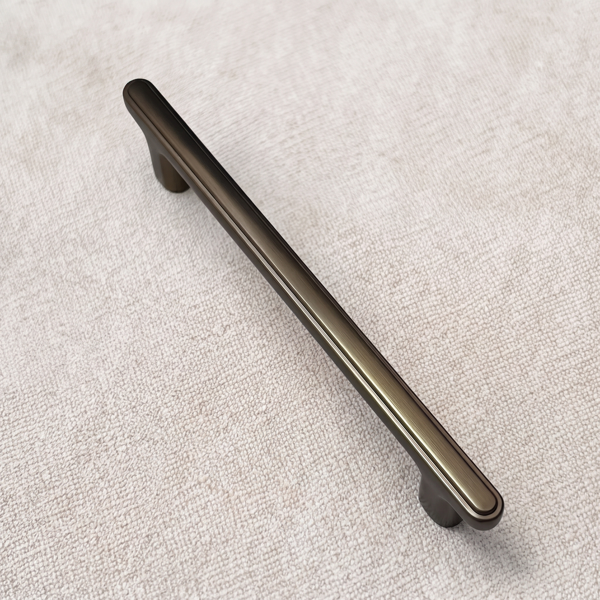 Coffee ridge-top bridge cabinet pull laid diagonally on pale linen, showing its raised ridge line