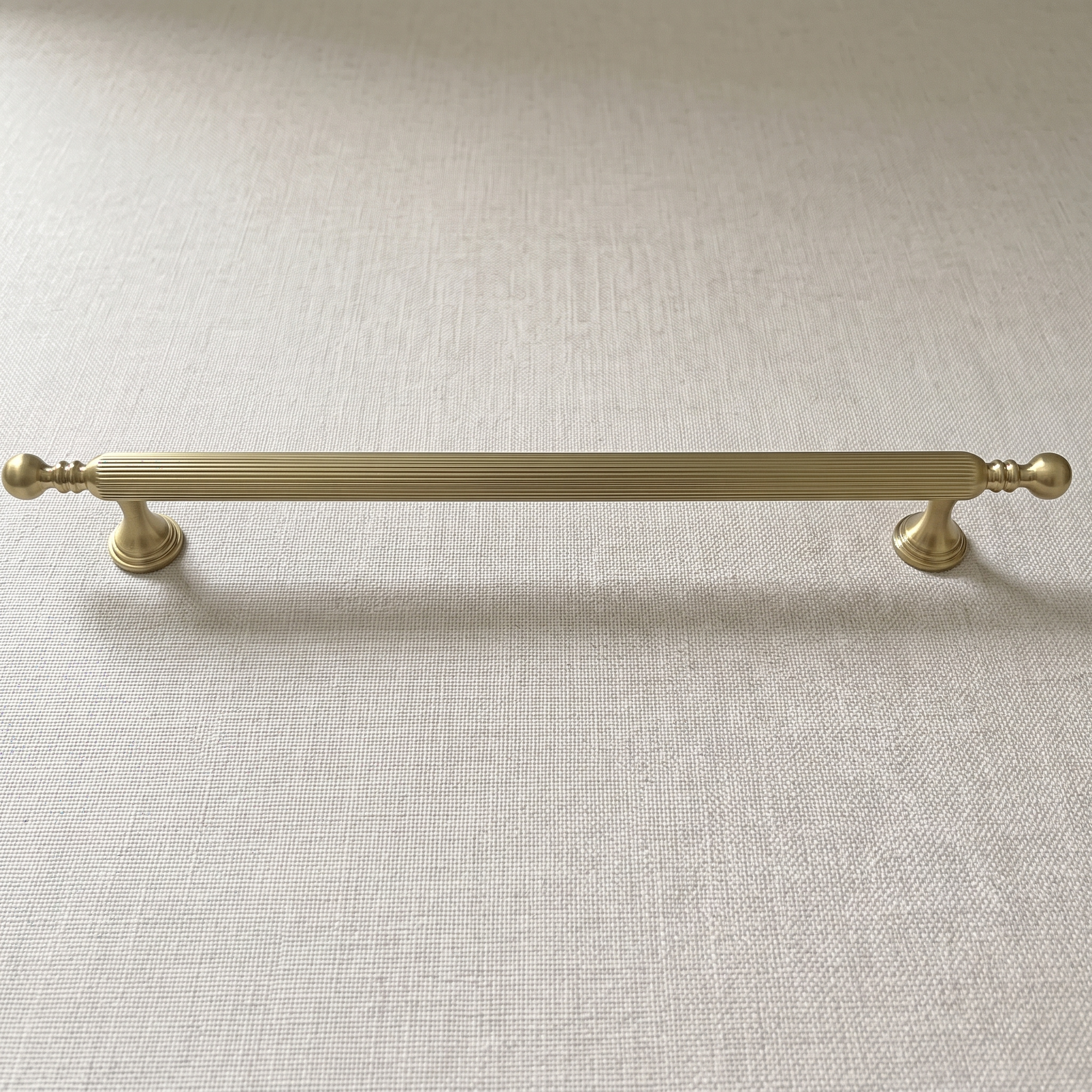 Front view of the straight-grain zinc cabinet pull in Brass Gold on a pale linen surface, with ball terminals, paired ring collars and bell feet in view