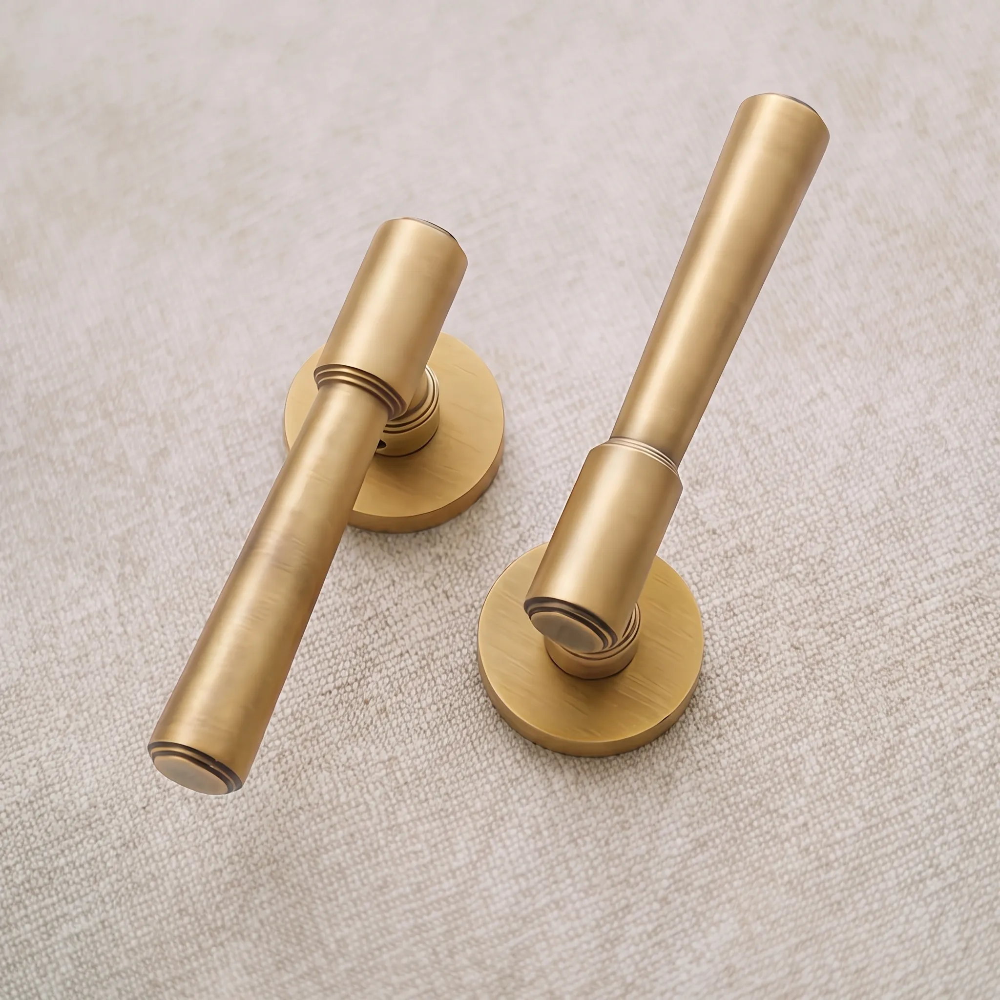 Two Aged Brass lever door handles on linen, showing the tapered cylindrical grip, the turned ring grooves at each collar and the circular rose plate
