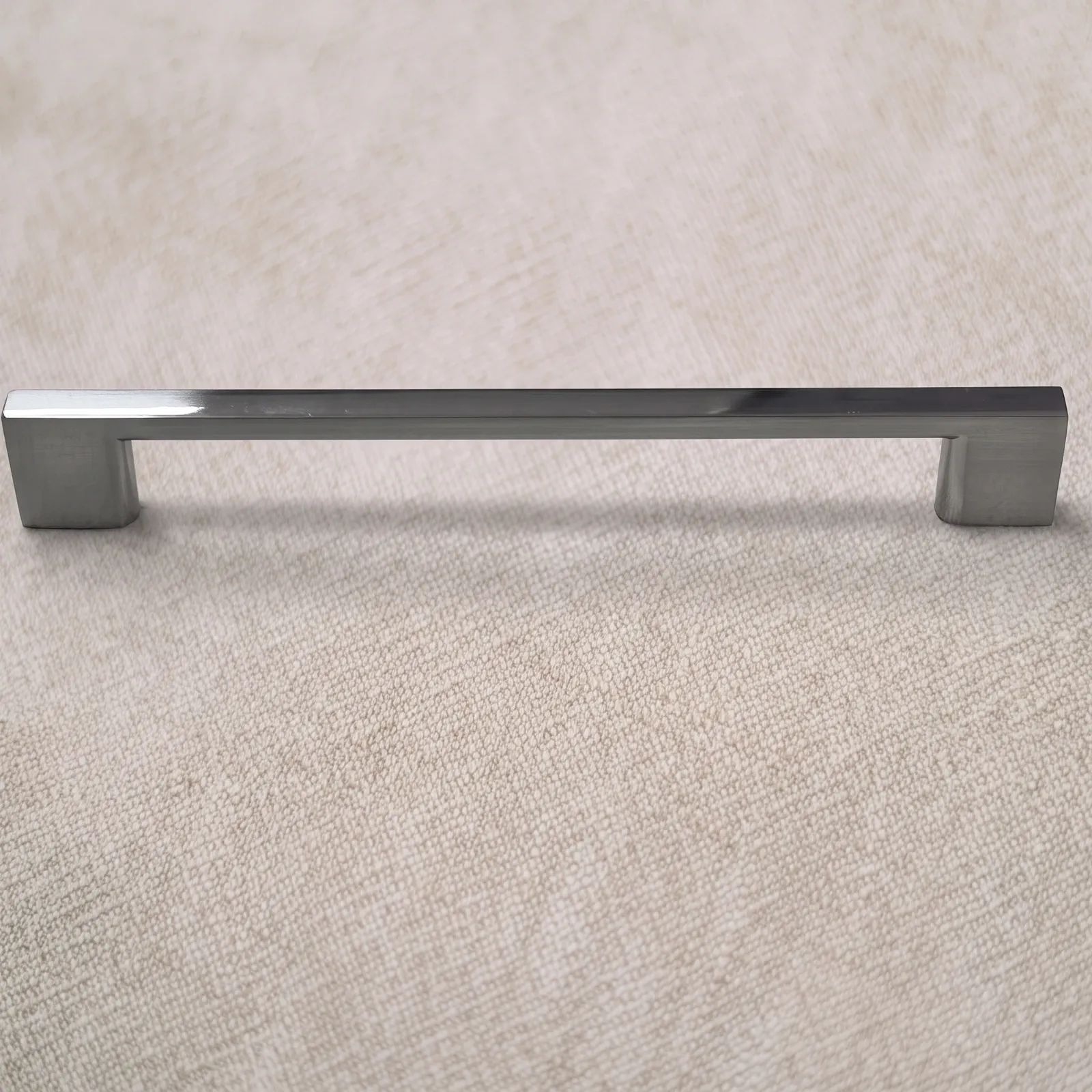 Straight-on view of a gunmetal wide flat bar pull with squat block foot terminals lying on linen.