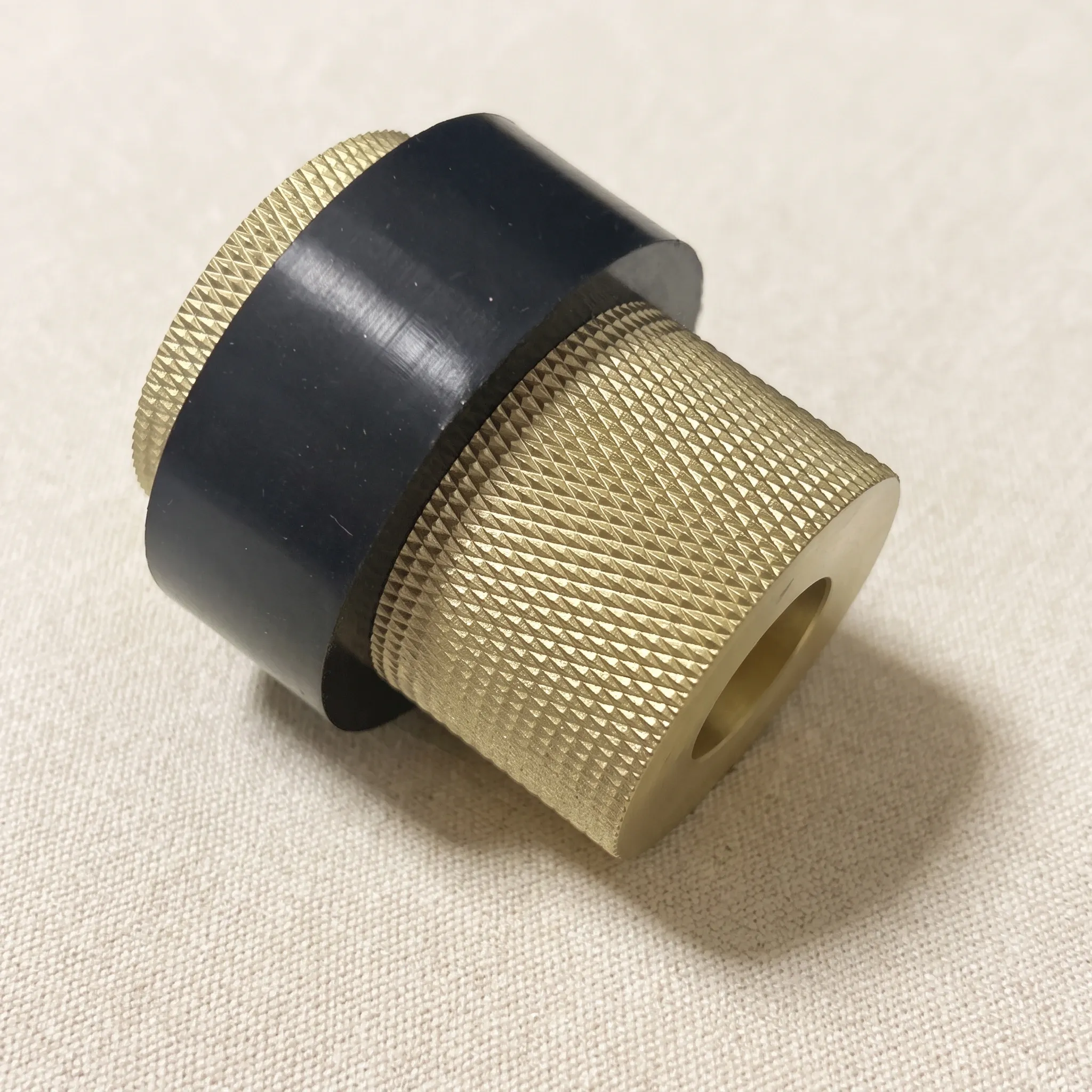 The Brass Gold knurled door stop resting on its side on a woven studio surface, with the knurled bands and black waist in profile.