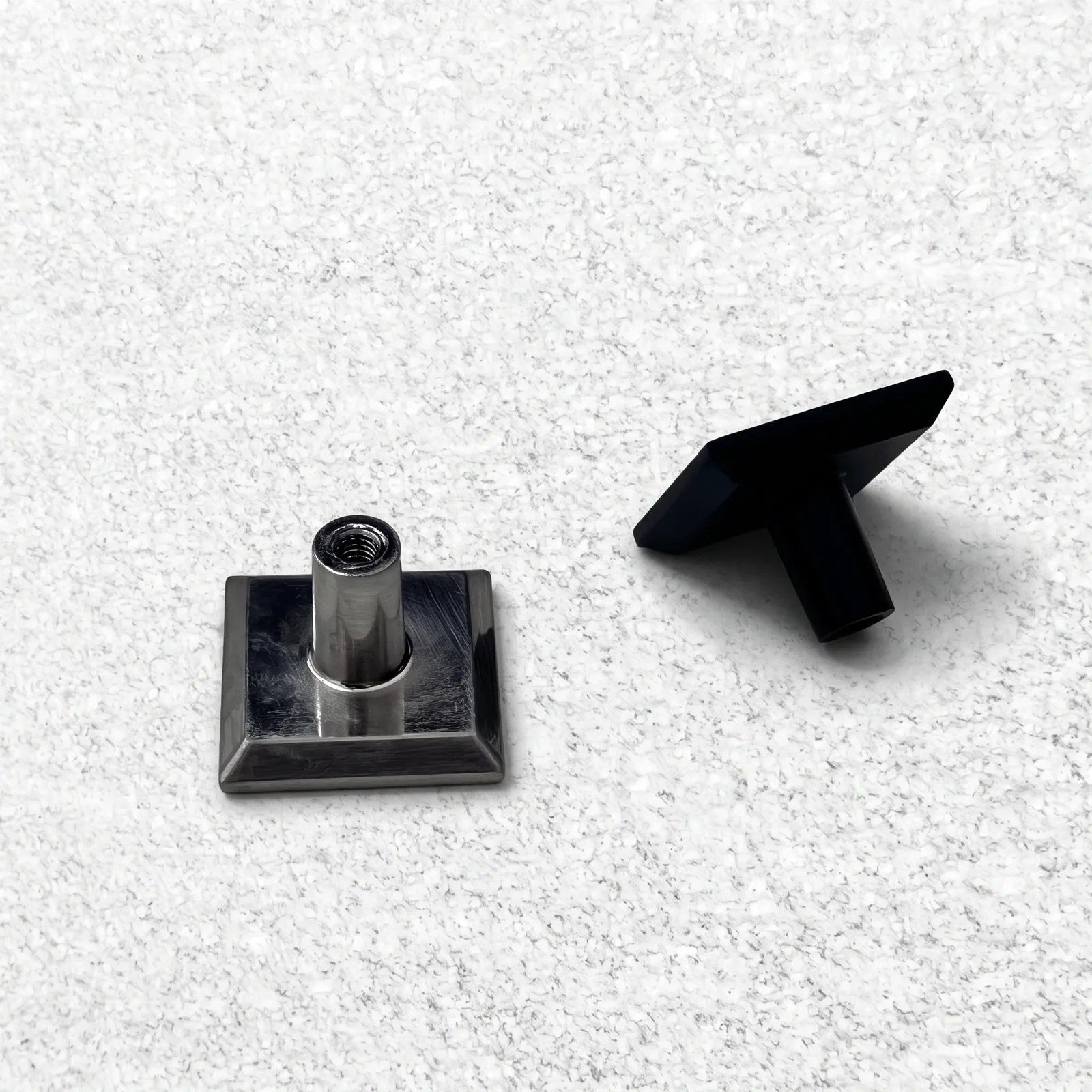 Square flat-plate cabinet knobs on a speckled ground, one shown upside down with its cylindrical stem and threaded bore.