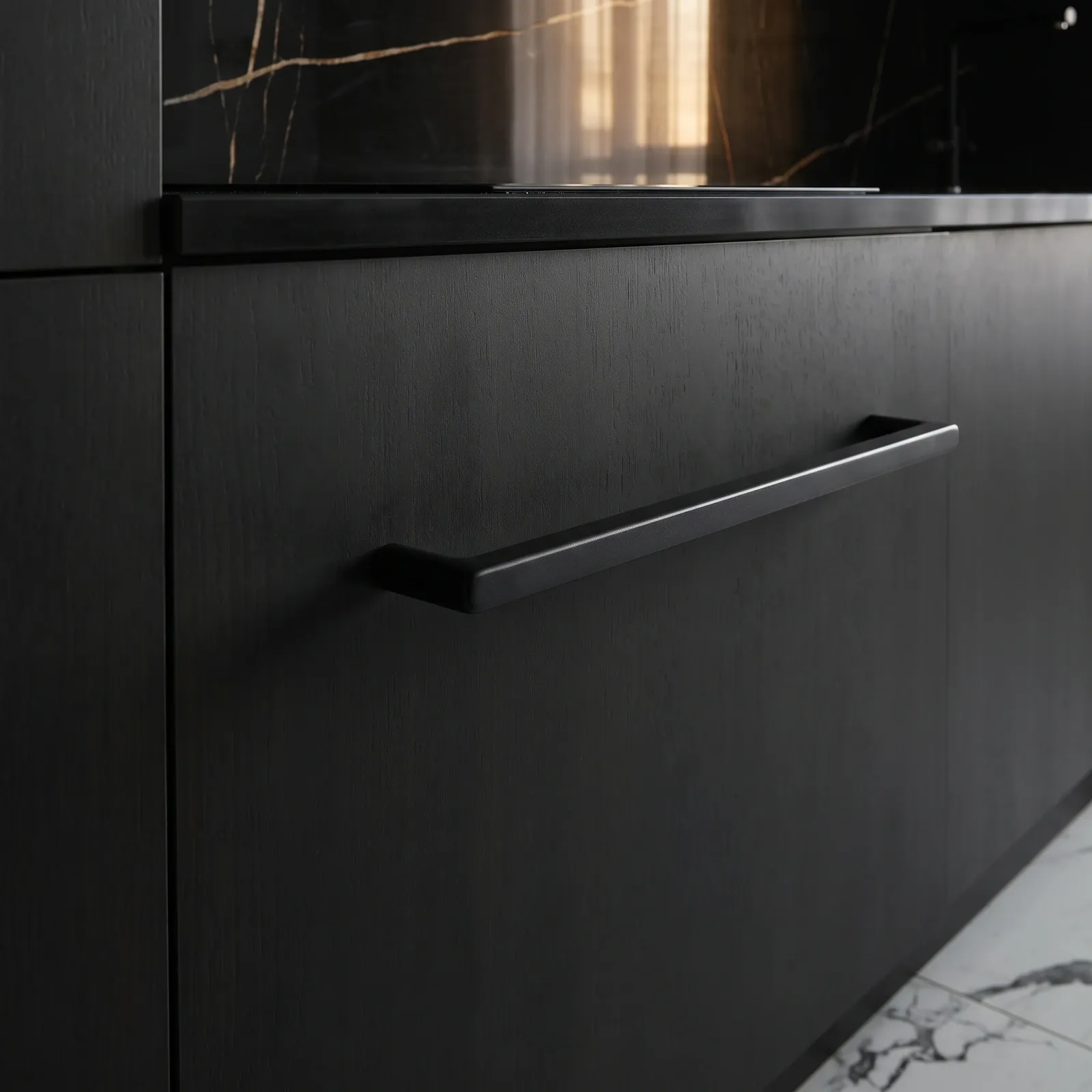 Matte Black square bar cabinet pull with cylindrical posts mounted on a black wood-grain kitchen drawer front beside a marble worktop.