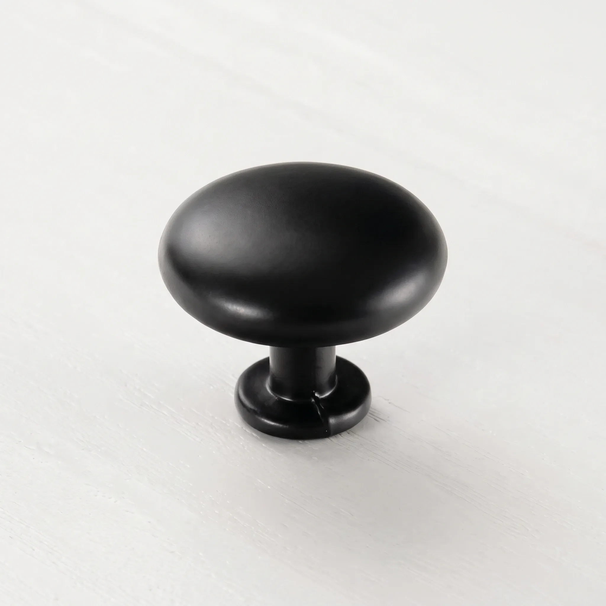Angled view of the matte black round mushroom cabinet knob showing its domed head, cylindrical stem and flared base plate
