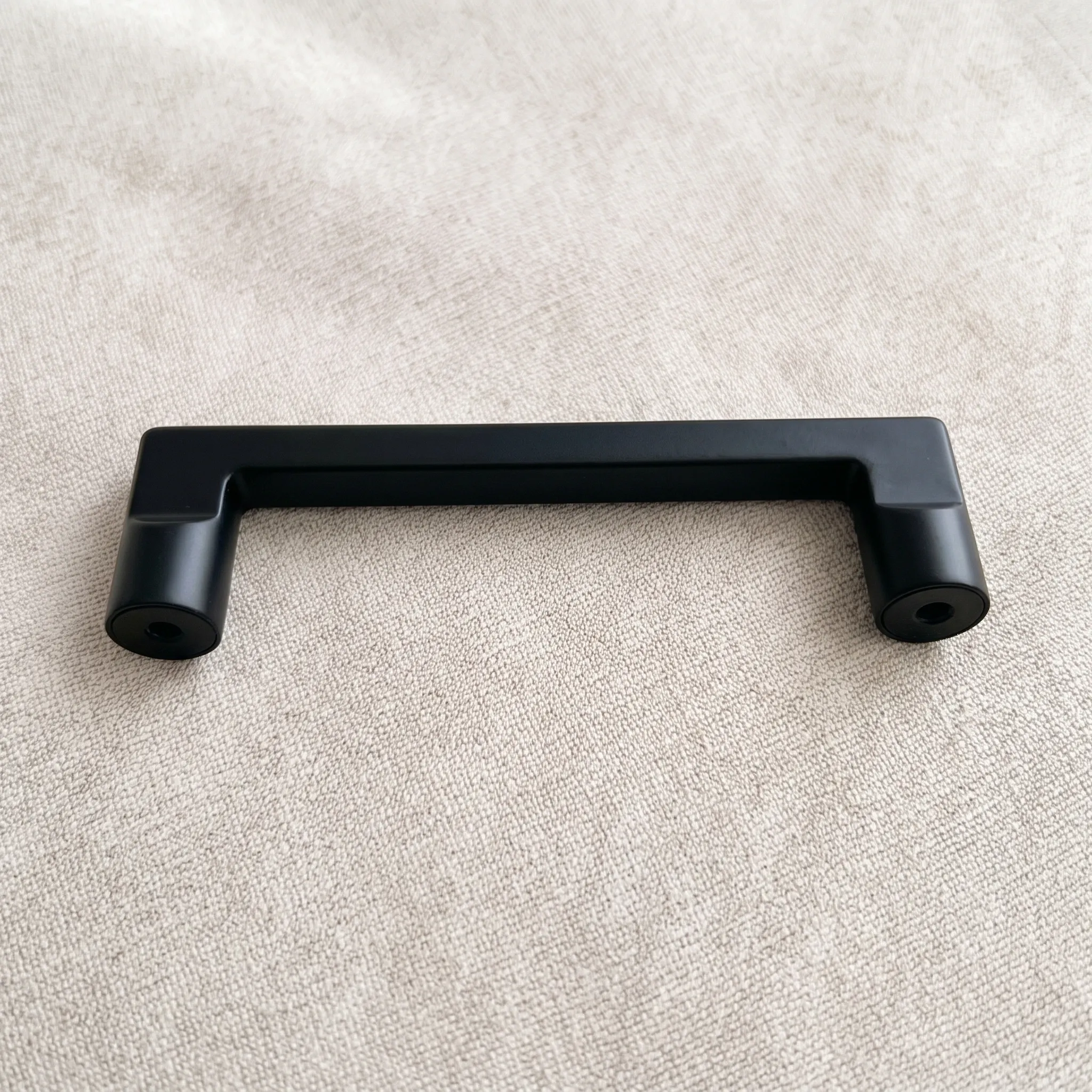 Matte black arch cabinet pull on a linen background showing the rectangular bar and both cylindrical feet from the front