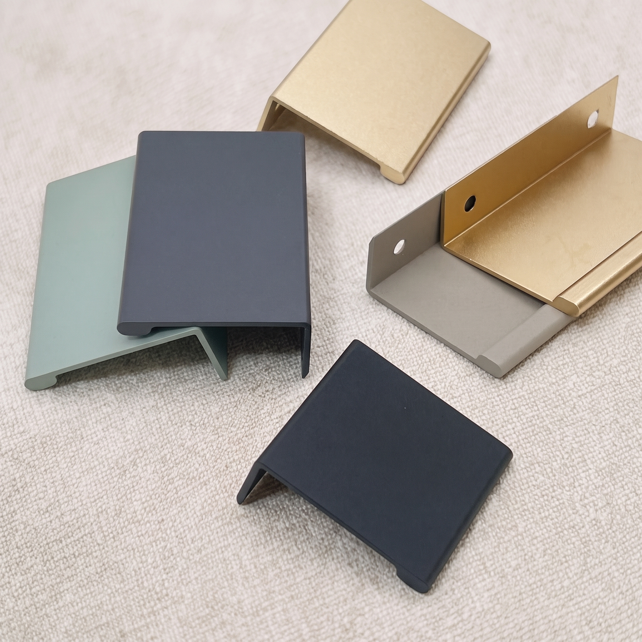 Six smooth-arc aluminum edge pulls in green, gunmetal, champagne gold, khaki, and matt black arranged on a pale beige fabric surface.
