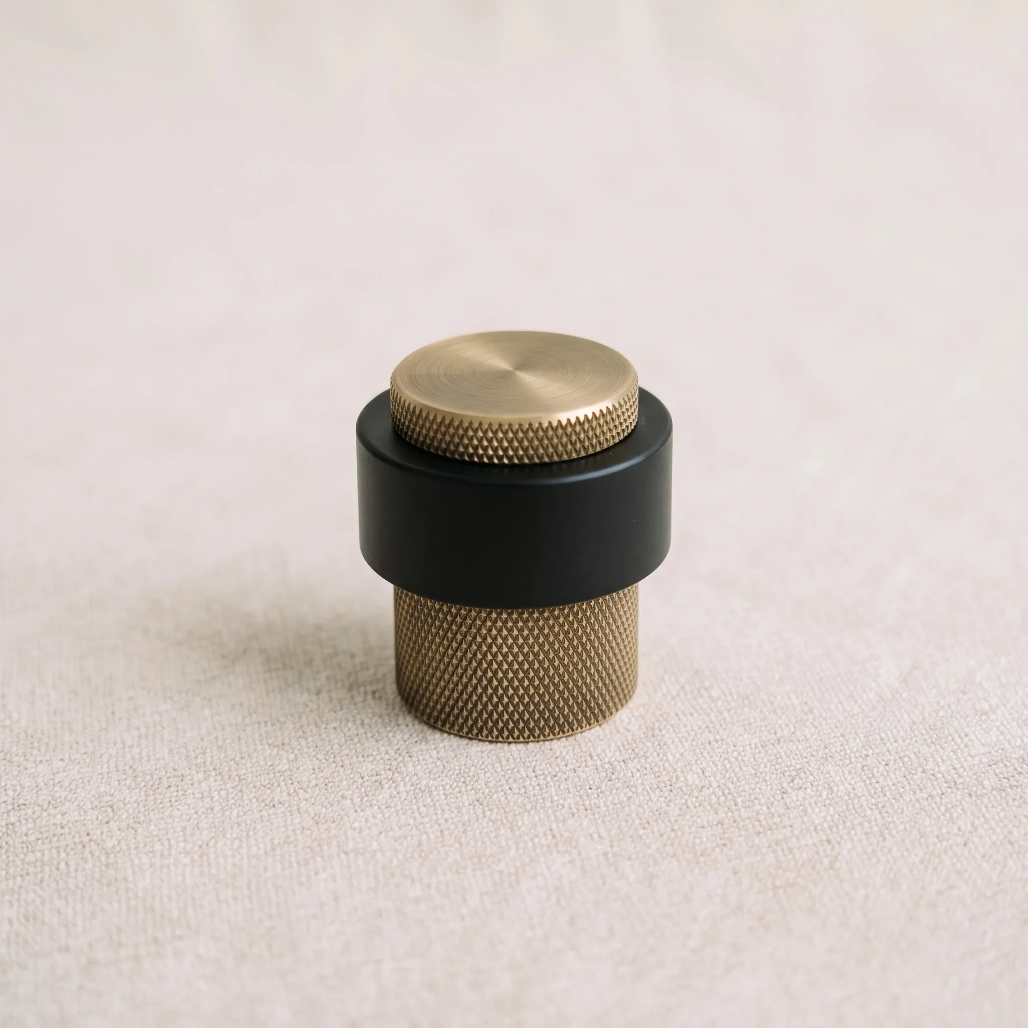 Eye-level view of the Brass Gold knurled door stop with its two-tone body against a plain light studio backdrop.