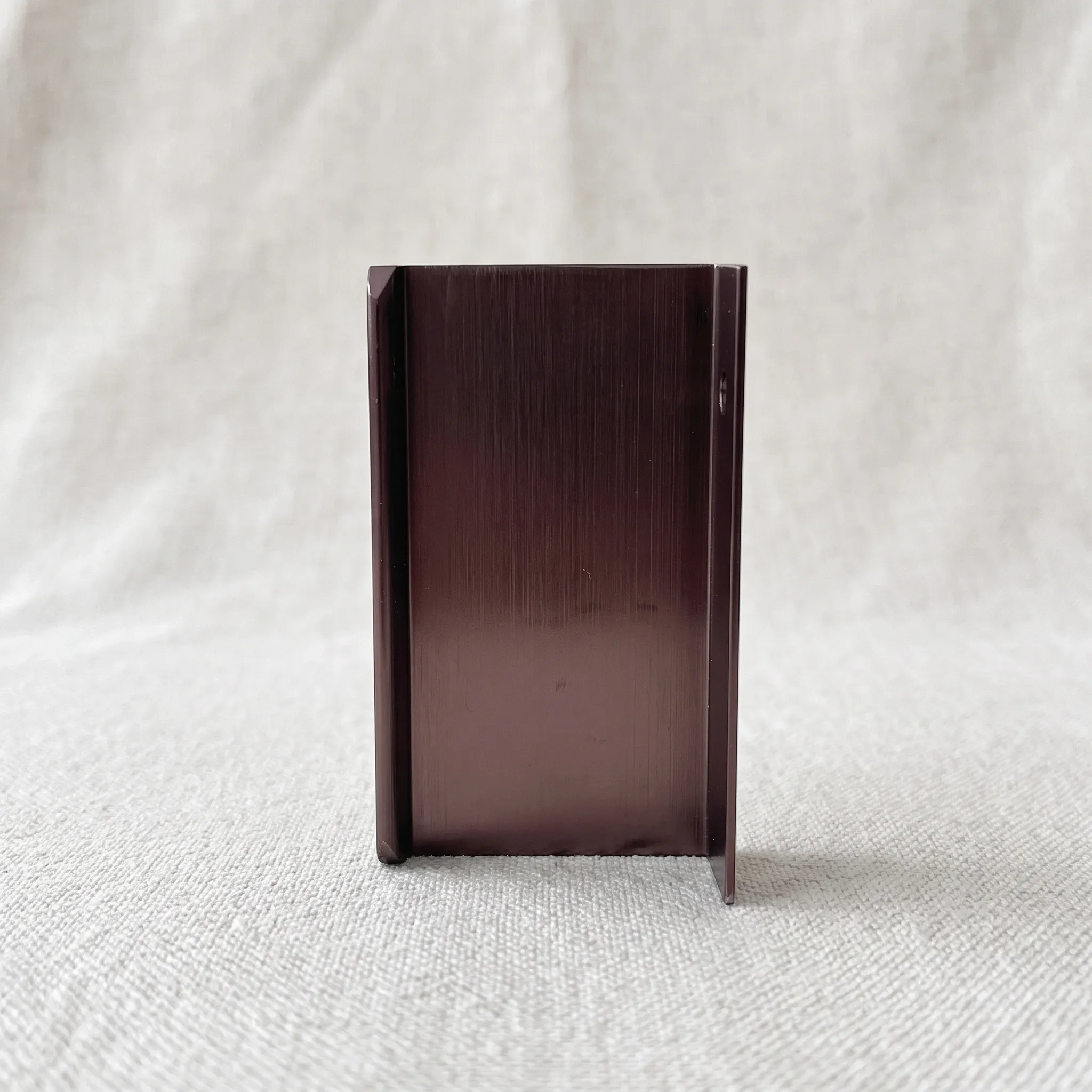 End-on view of the aluminum edge pull standing on linen, showing the folded upstand of the L profile