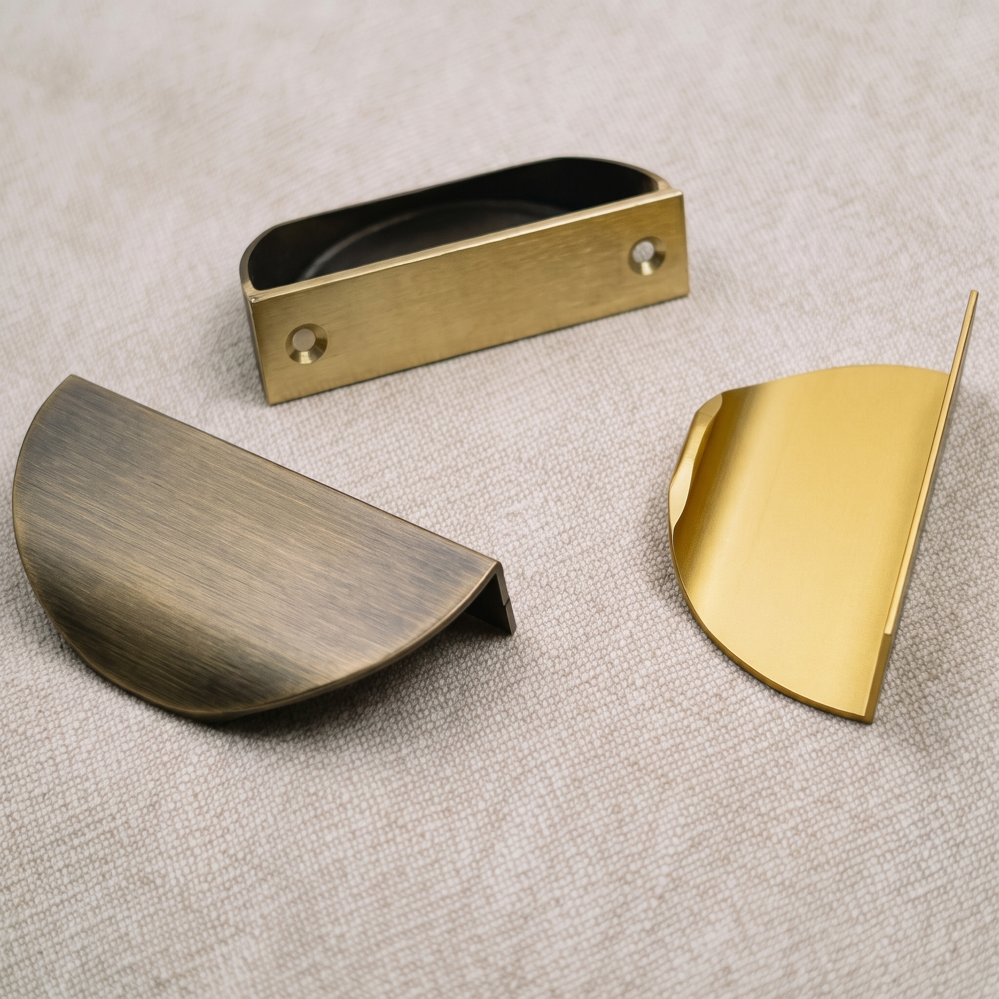 Three half-moon edge pulls arranged on pale linen, one turned to show its rear mounting lip and two screw holes