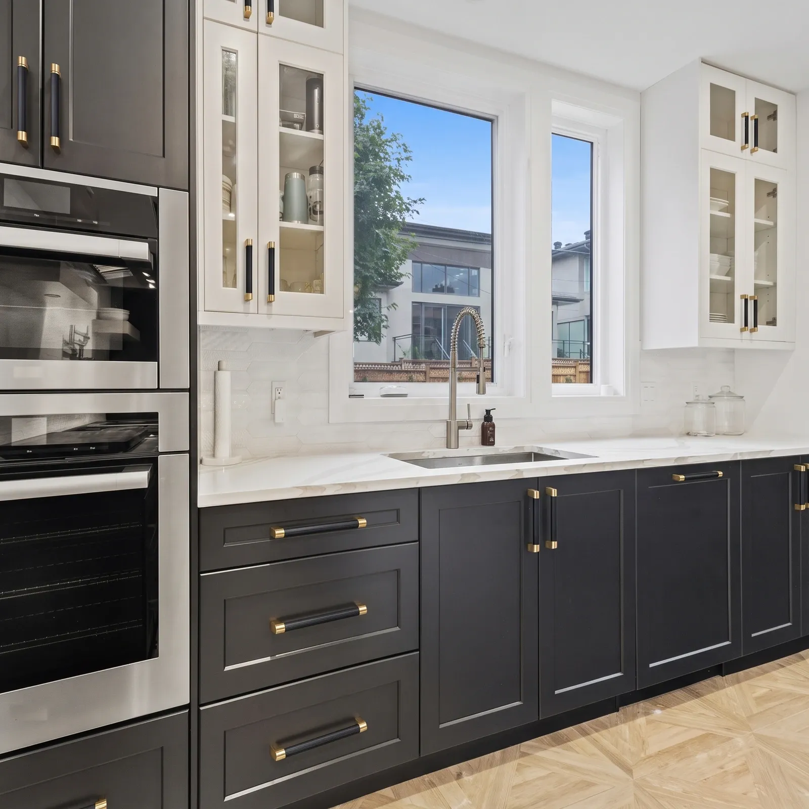 Charcoal and white shaker kitchen cabinets fitted with color-blocked D-profile pulls that have dark grooved grips and gold collars