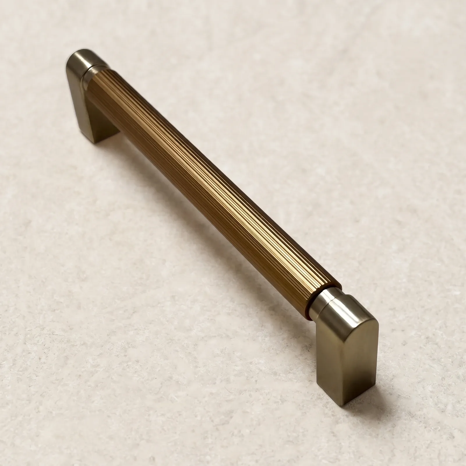 Brass gold D-profile cabinet pull with a grooved round grip standing on a cream backdrop