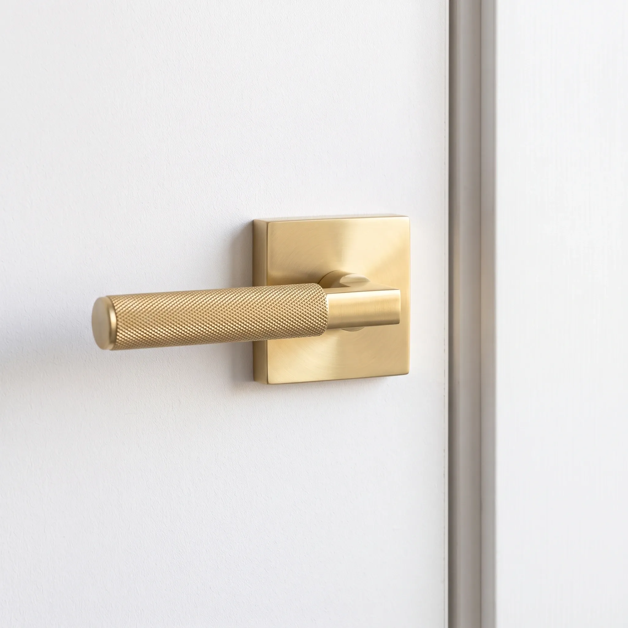 Gold knurled privacy door handle lock set with a square rose plate fitted on a white painted interior door