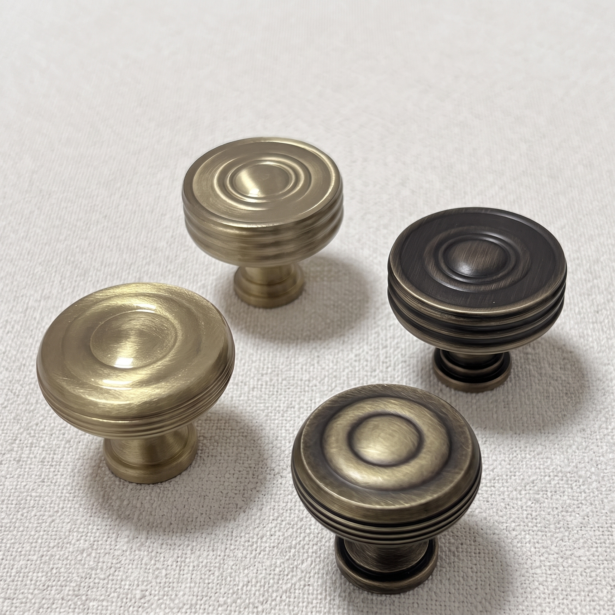 Four circular knobs from the family arranged on pale linen, showing concentric ring faces and banded sides