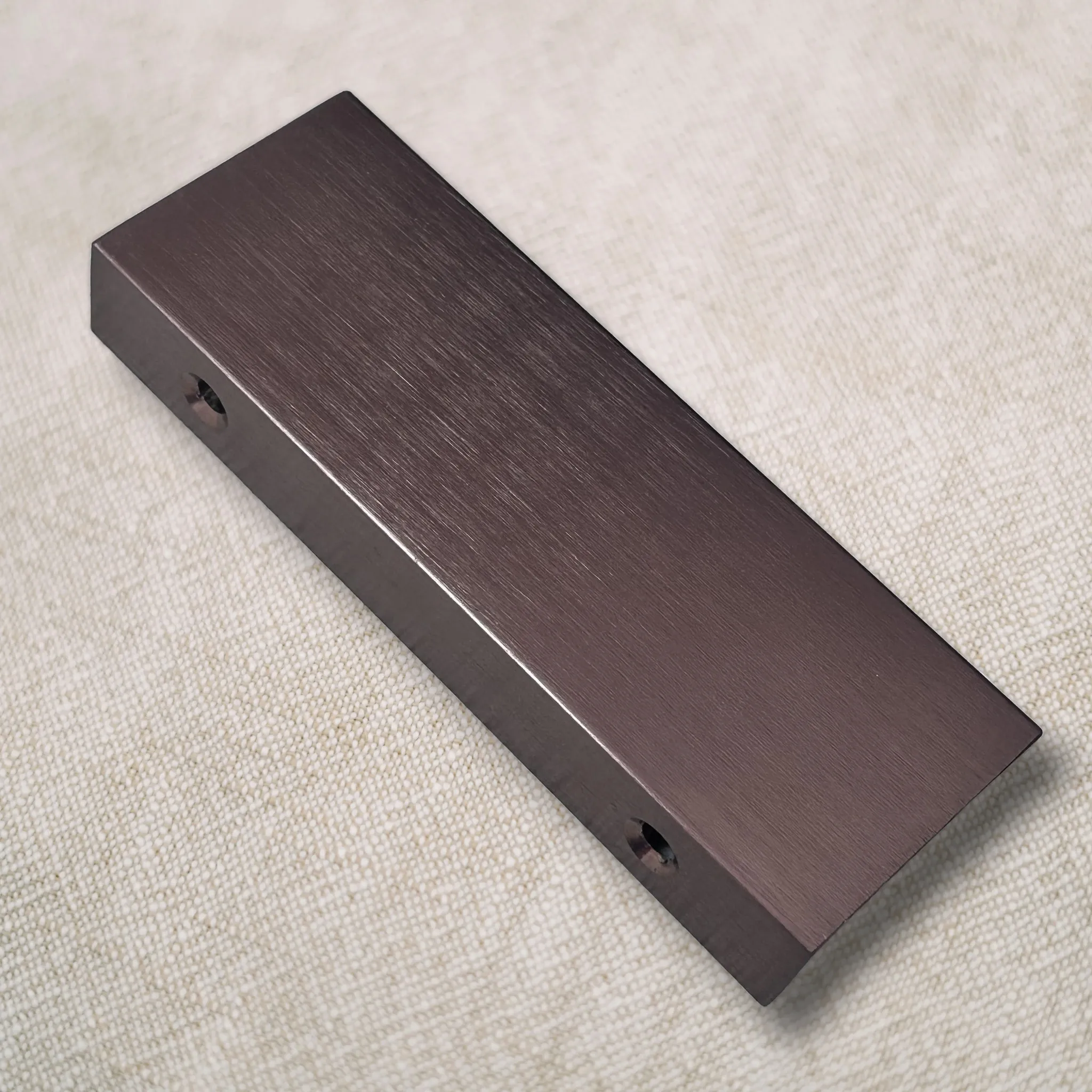 Angled top view of the edge pull on linen showing countersunk holes drilled through the long mounting face