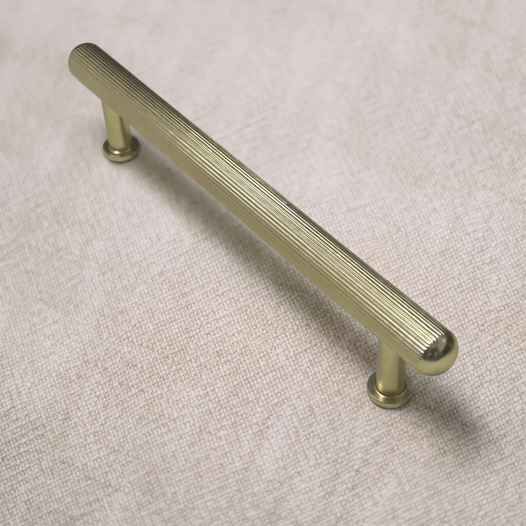 Angled view of a Brush Gold ribbed aluminum T-bar cabinet pull with a full-length ribbed cylindrical bar, domed ends and two flared collar posts on round base plates