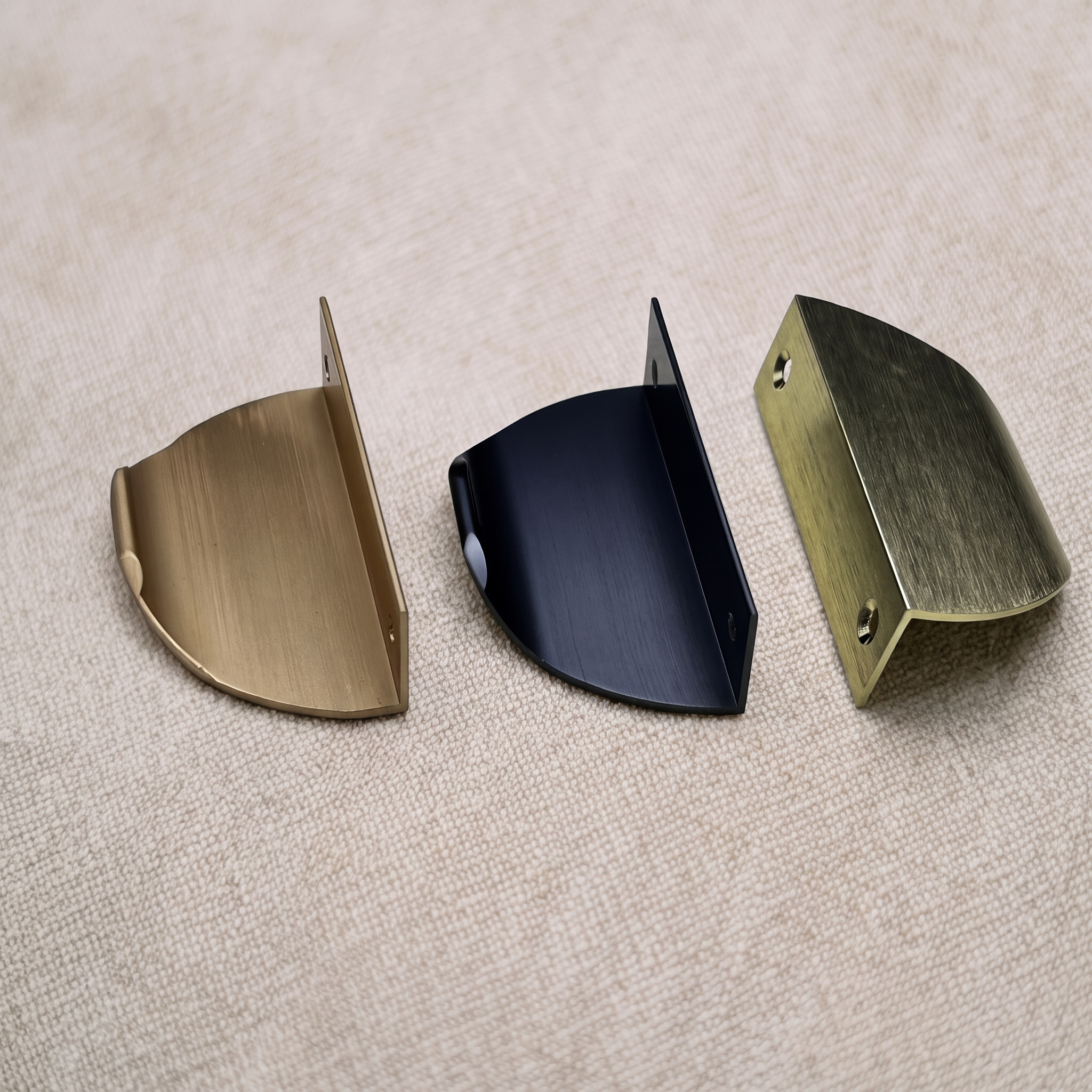 Three half-moon edge pulls standing in a row on pale linen, showing the thin arched profile and folded mounting lip