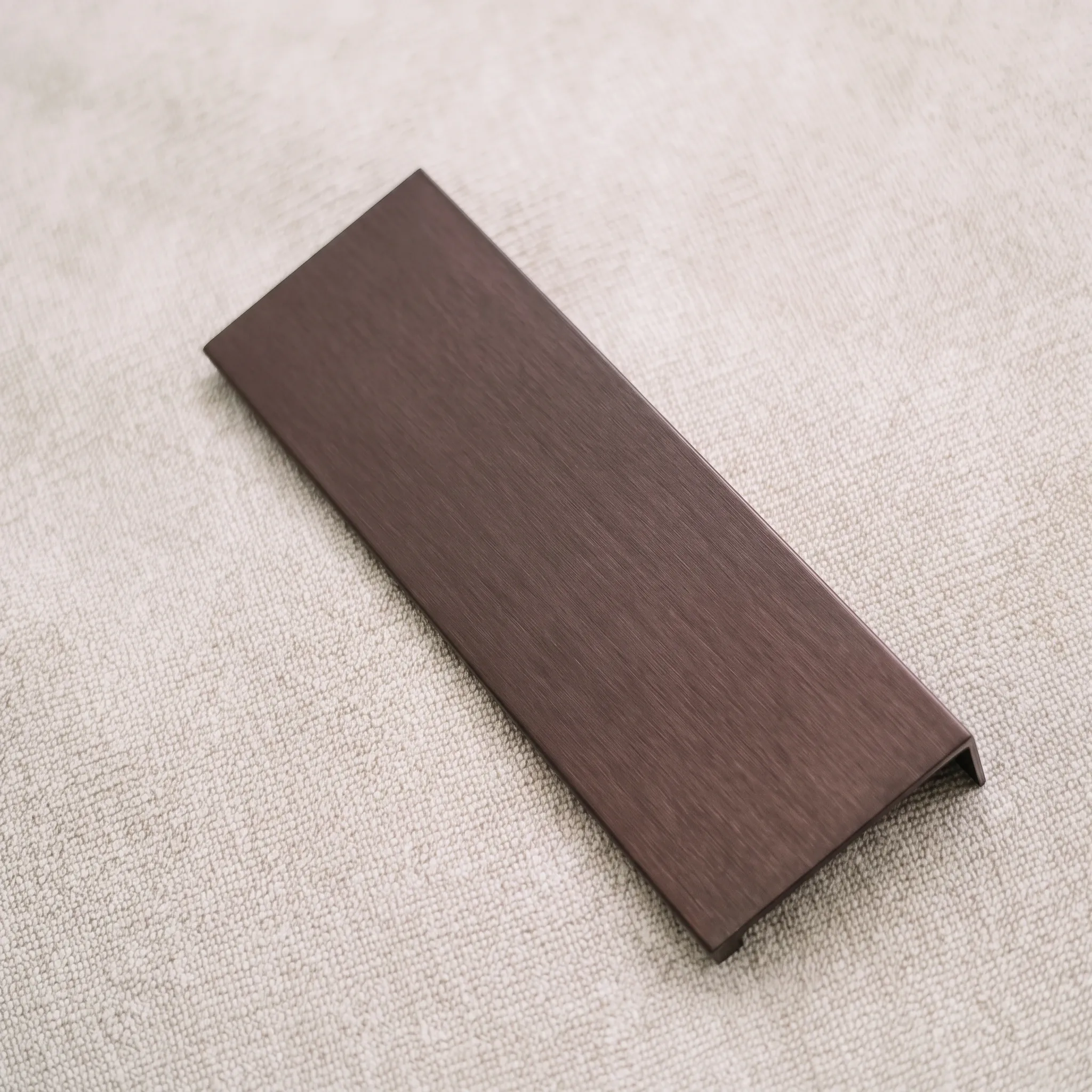 Side-mounted aluminum edge pull set diagonally on linen, with the folded return running along one long edge