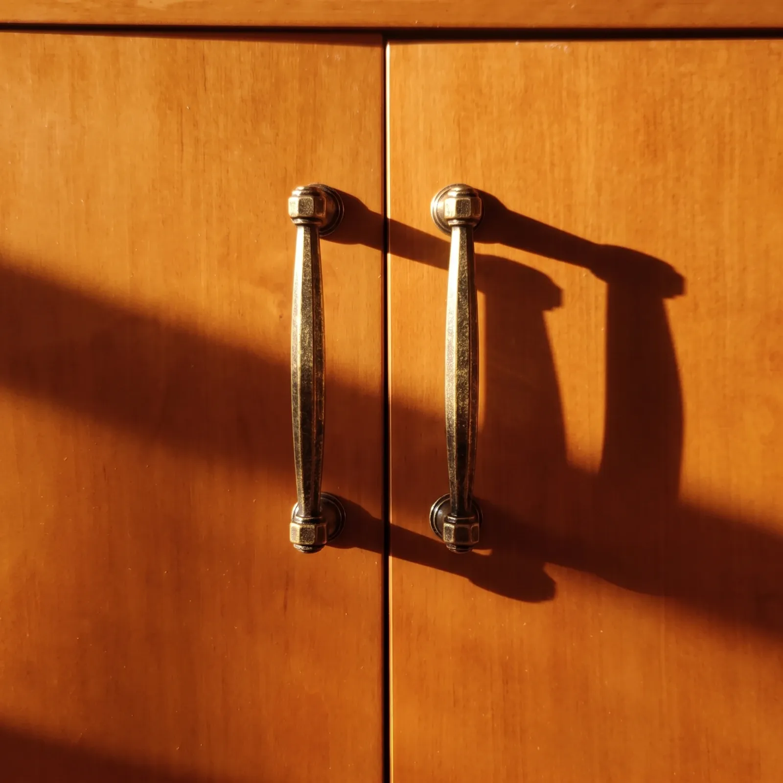 Two curved bow pulls with ringed collars mounted on warm wooden cabinet doors in sunlight