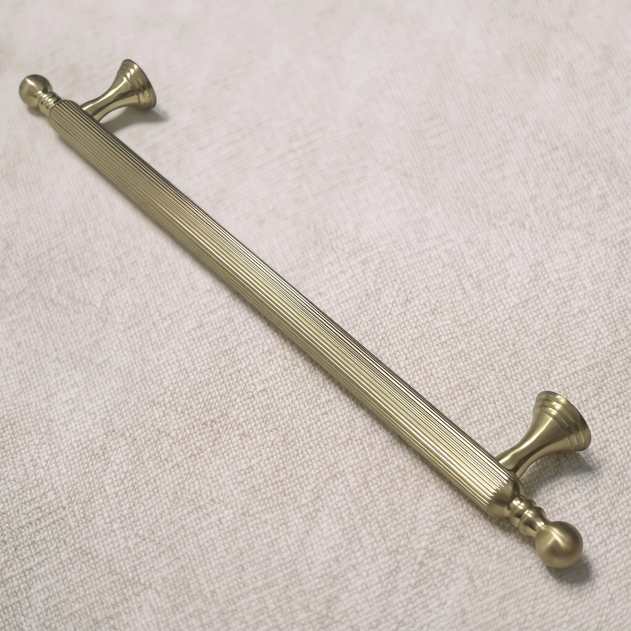 Angled view of the straight-grain zinc cabinet pull in Brass Gold from the opposite three-quarter side, resting on a pale linen surface