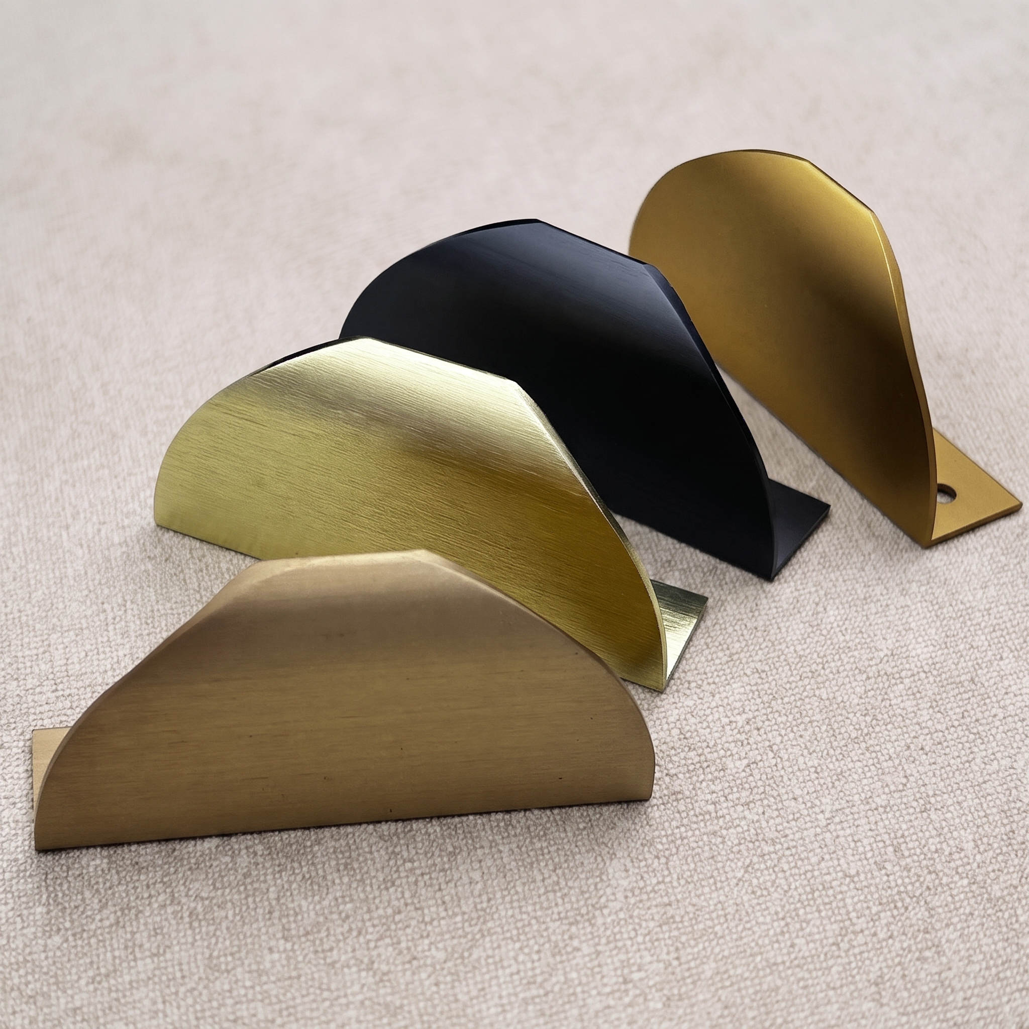 Four half-moon aluminum edge pulls standing on edge on pale linen, showing the folded rear lip and slim curved shells across the finish range