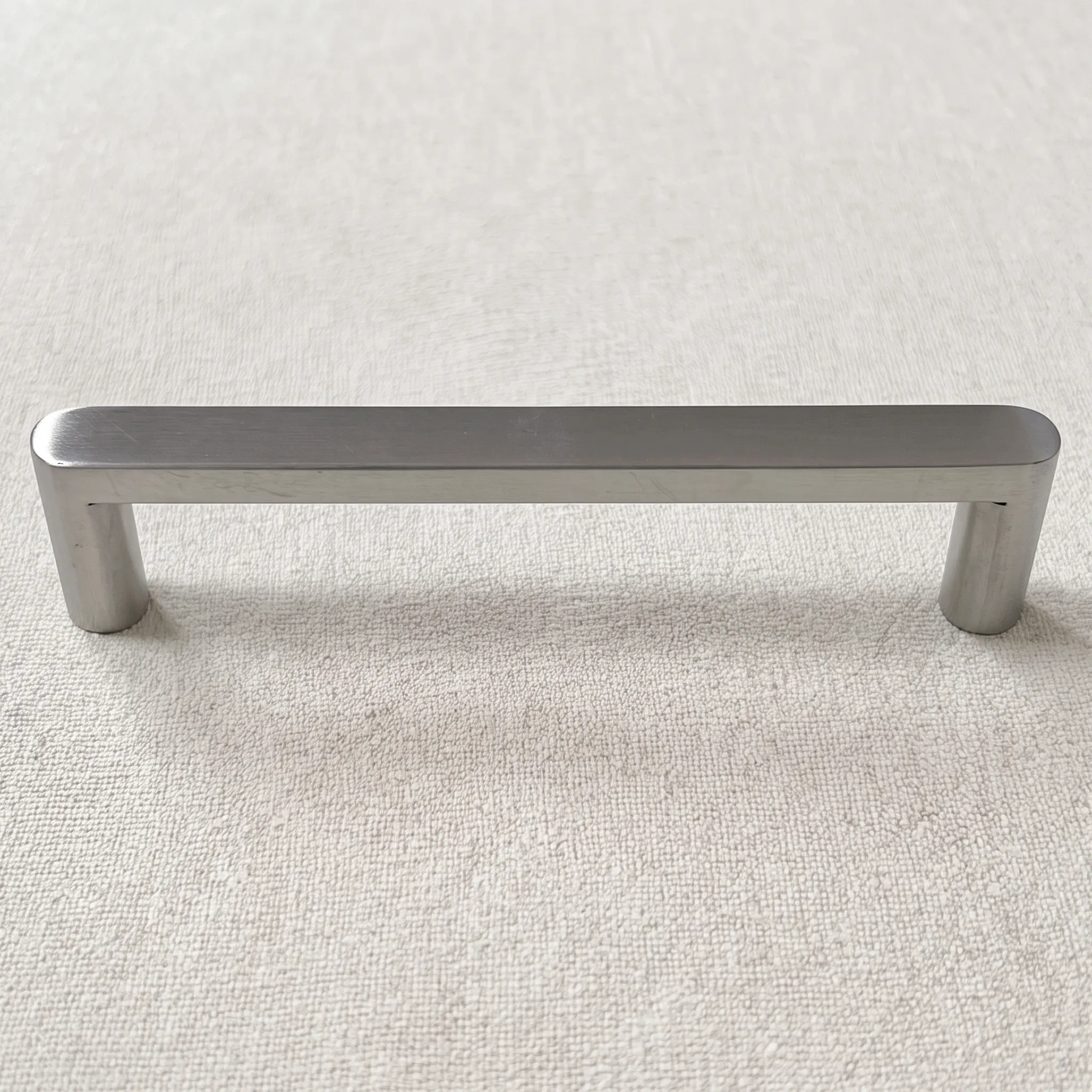 Straight-on view of the polished stainless steel flat-sided pull on round legs, resting on natural linen
