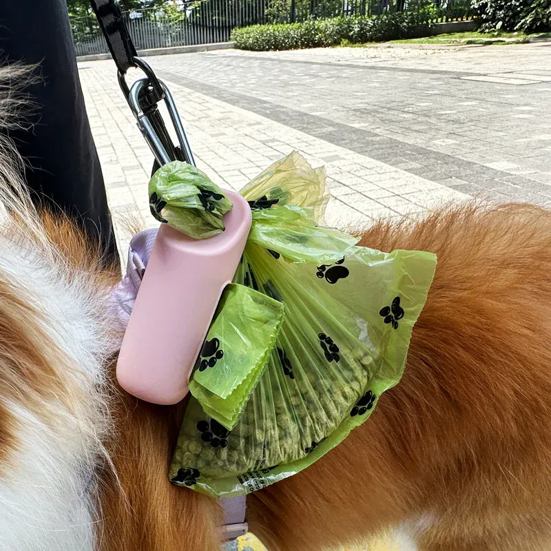 Pink silicone poop bag dispenser with green paw-print bags clipped to a walking dog
