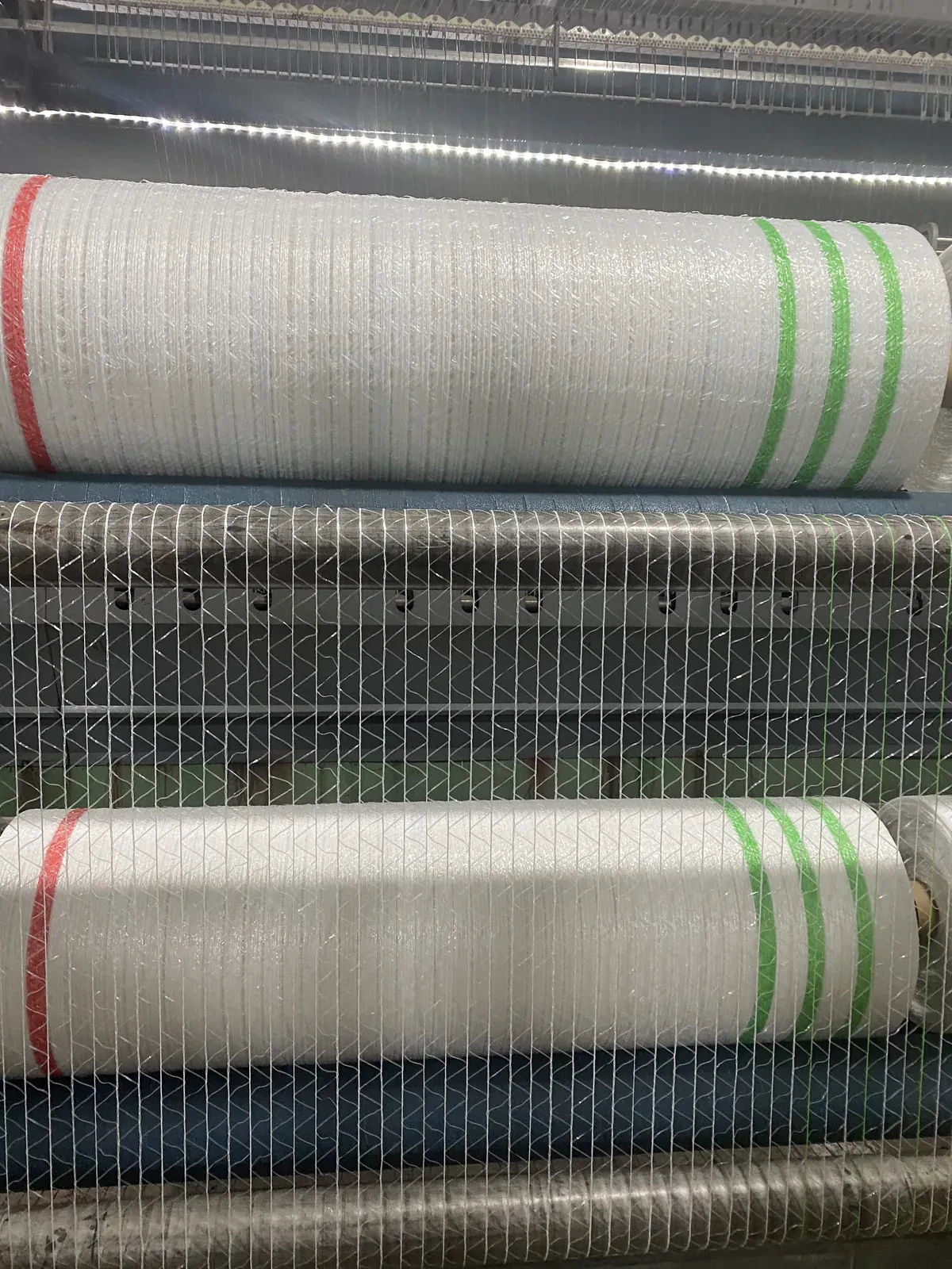 White netting passing over rollers beneath striped net rolls on production equipment