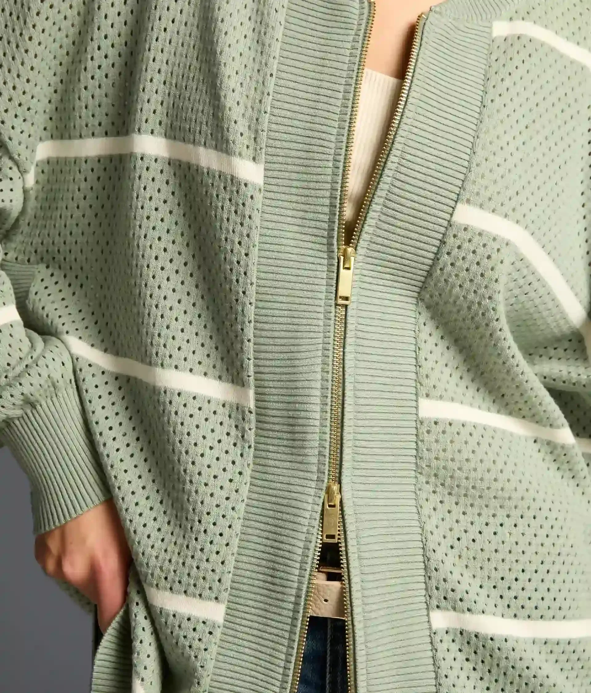 Close-up of the gold zipper and ribbed placket on the sage green open-weave zip-front cardigan
