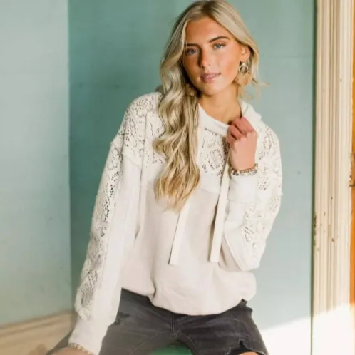 Model seated by a window wearing the cream lace-trim hoodie