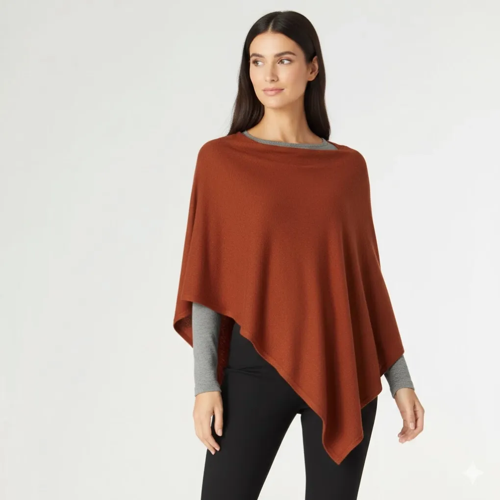 Front view of a rust terracotta knit poncho with an asymmetric drape hem