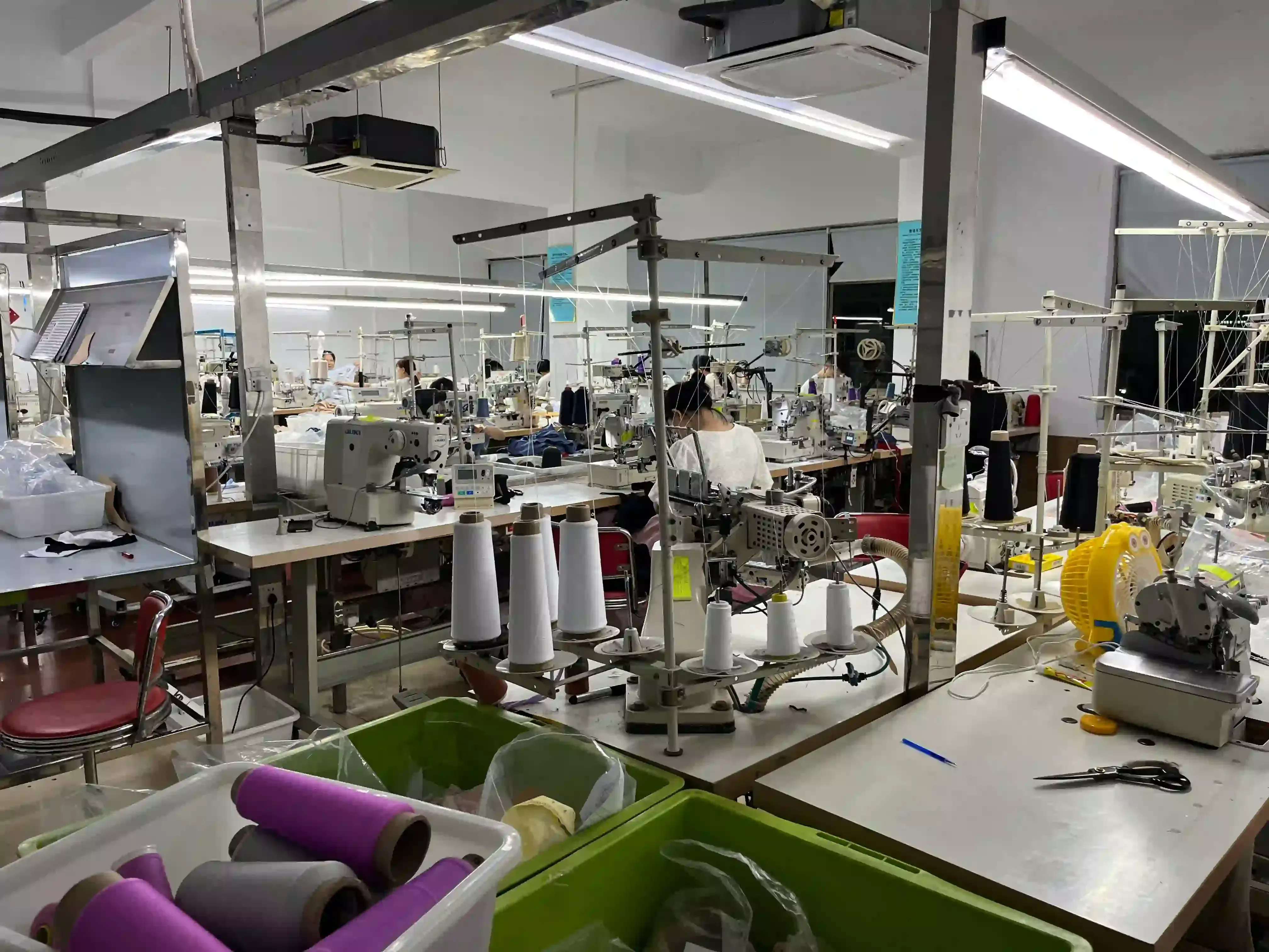Sewing stations with thread cones and green storage bins inside the knitwear workshop
