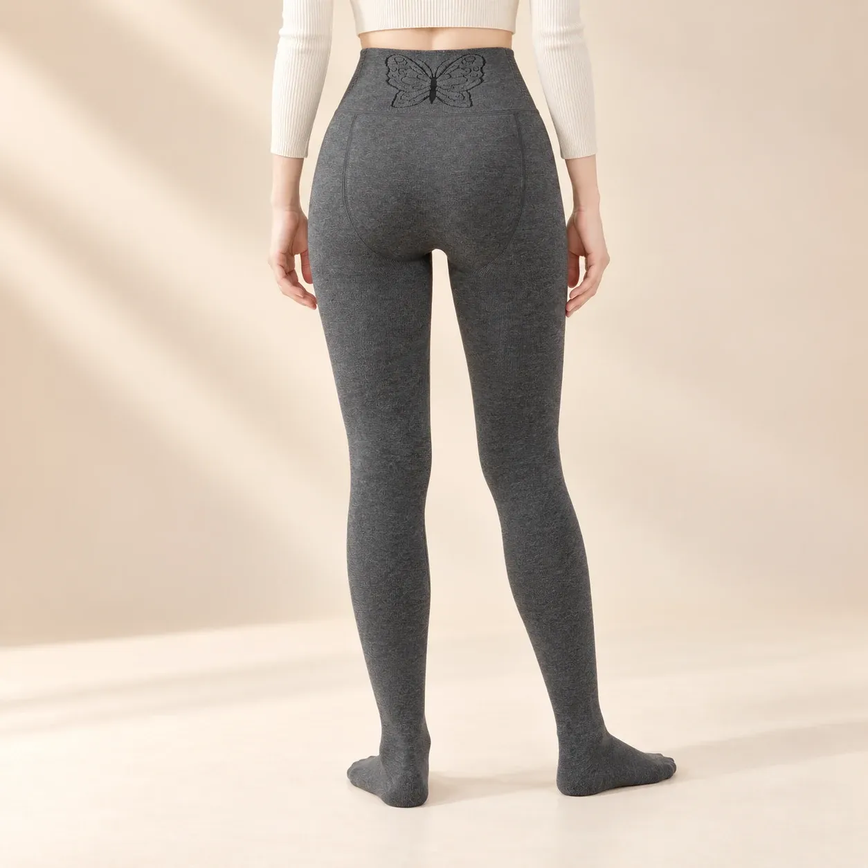 Back view of charcoal grey fleece-lined footed leggings with a butterfly-pattern waistband and curved rear panel seams.
