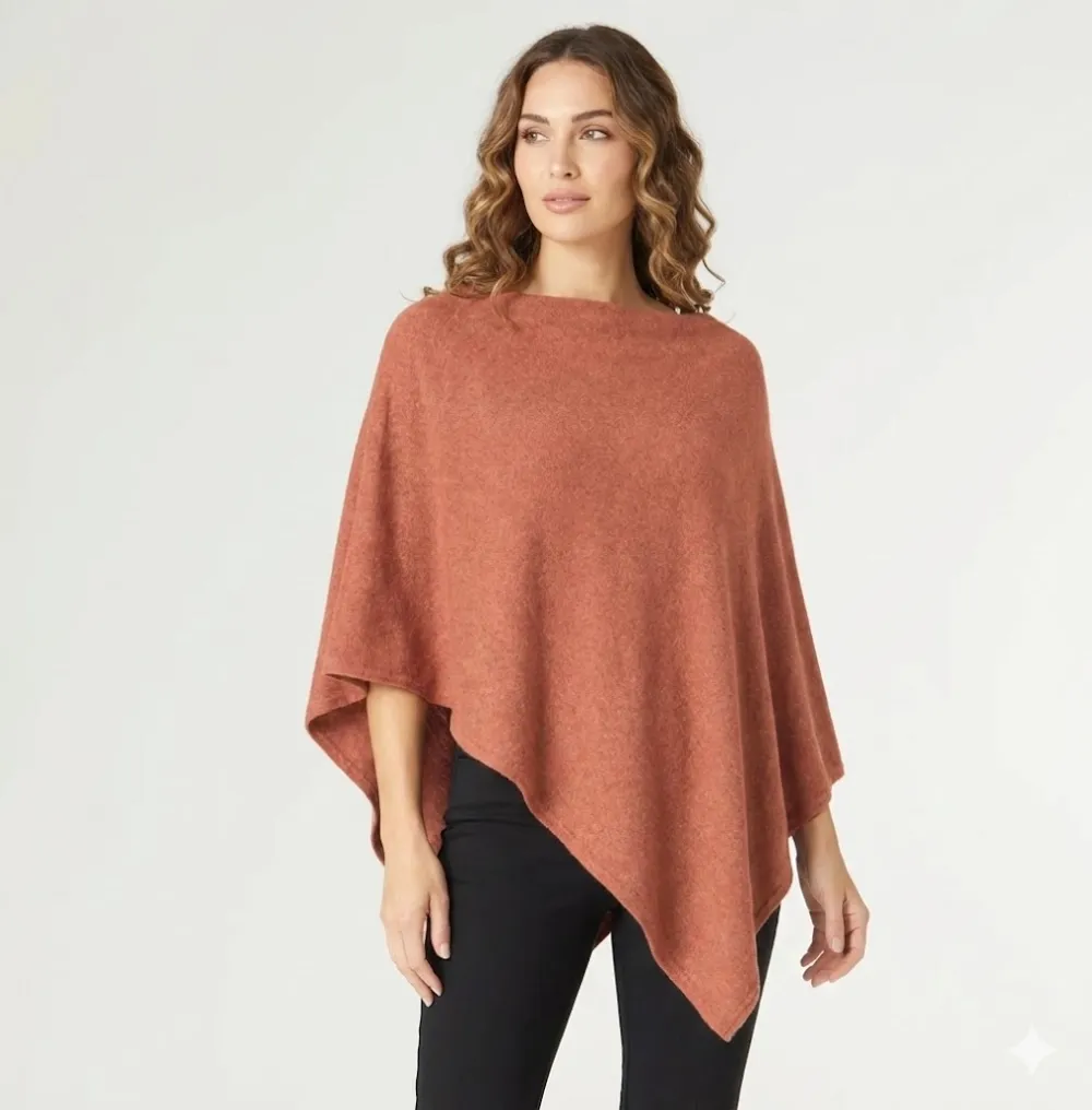 Three-quarter view of the rust terracotta knit poncho showing the draped asymmetric hem