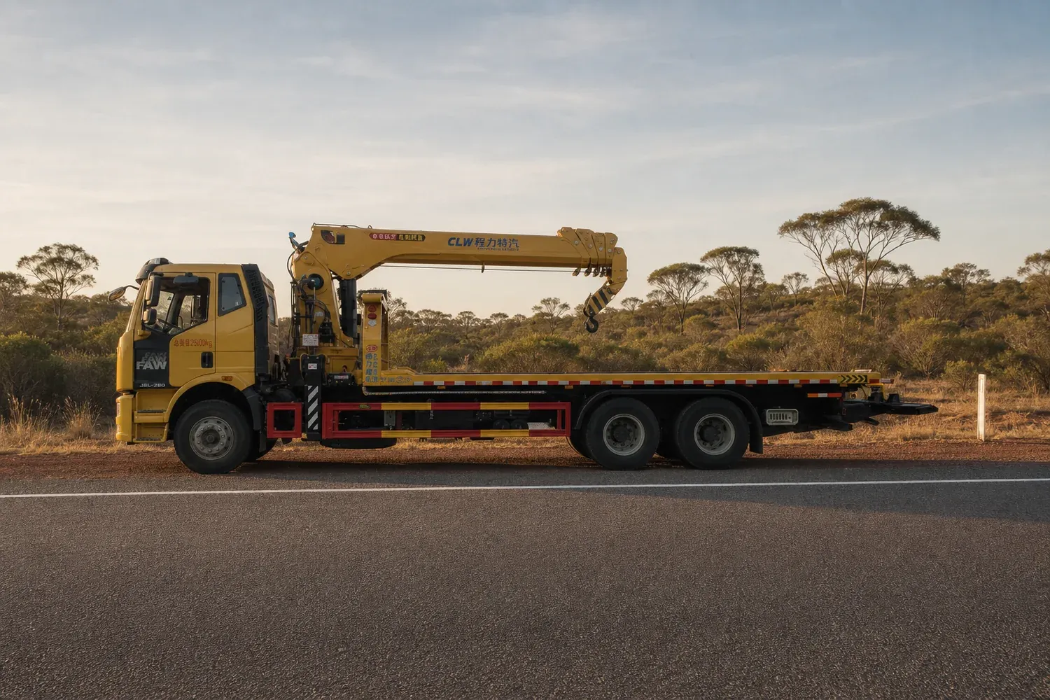 Crane-equipped recovery lorry in side profile on a highway shoulder beside a red-earth verge, importing a crane truck into Kenya