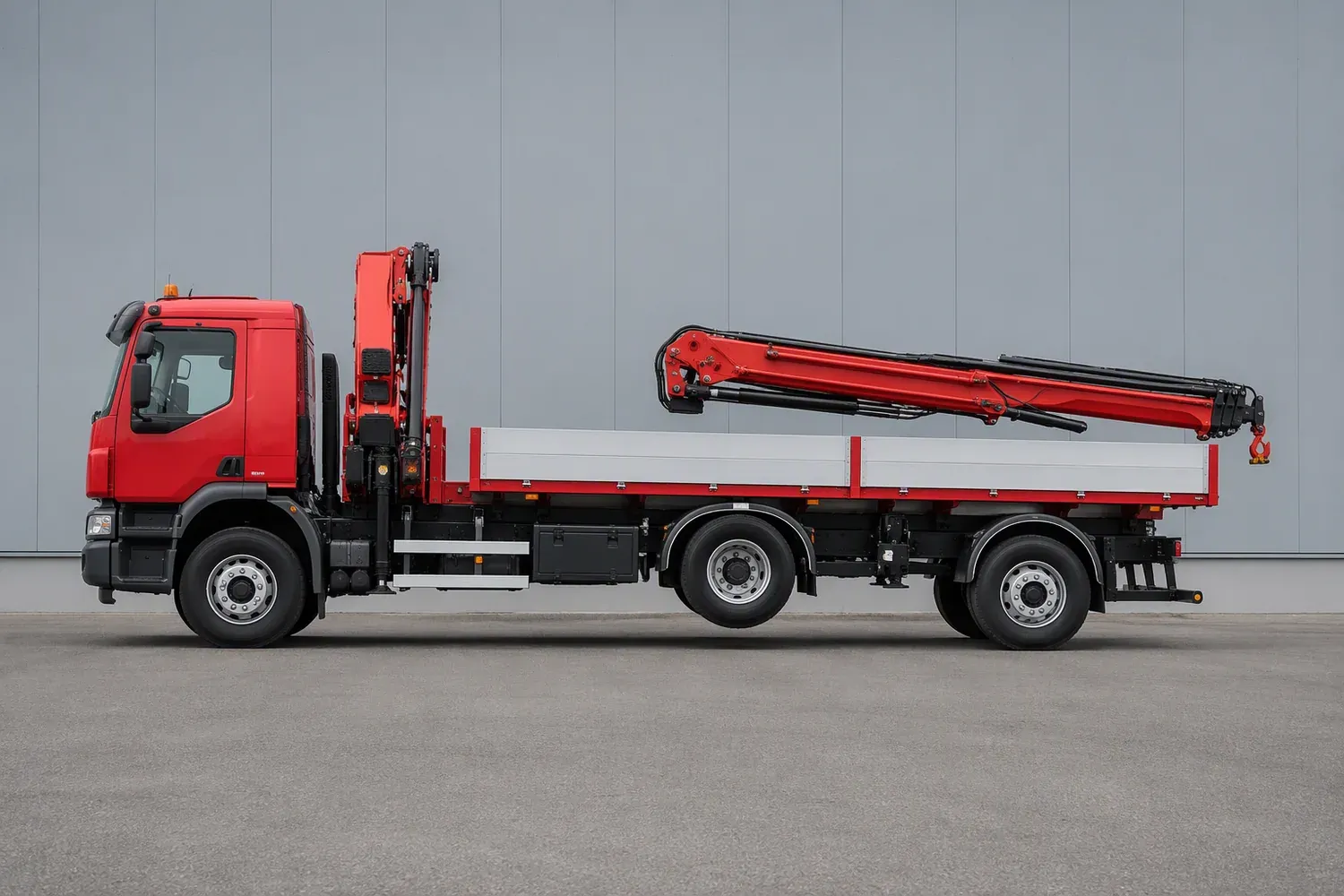 Side view of a three-axle truck-mounted crane lorry with the crane boom folded and stowed rearward over the flatbed deck
