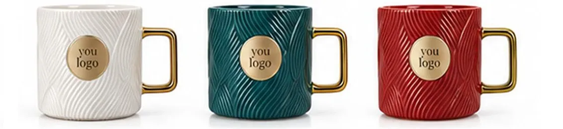 Cream, green and red ceramic mugs with textured sides, square handles and circular logo placeholders.