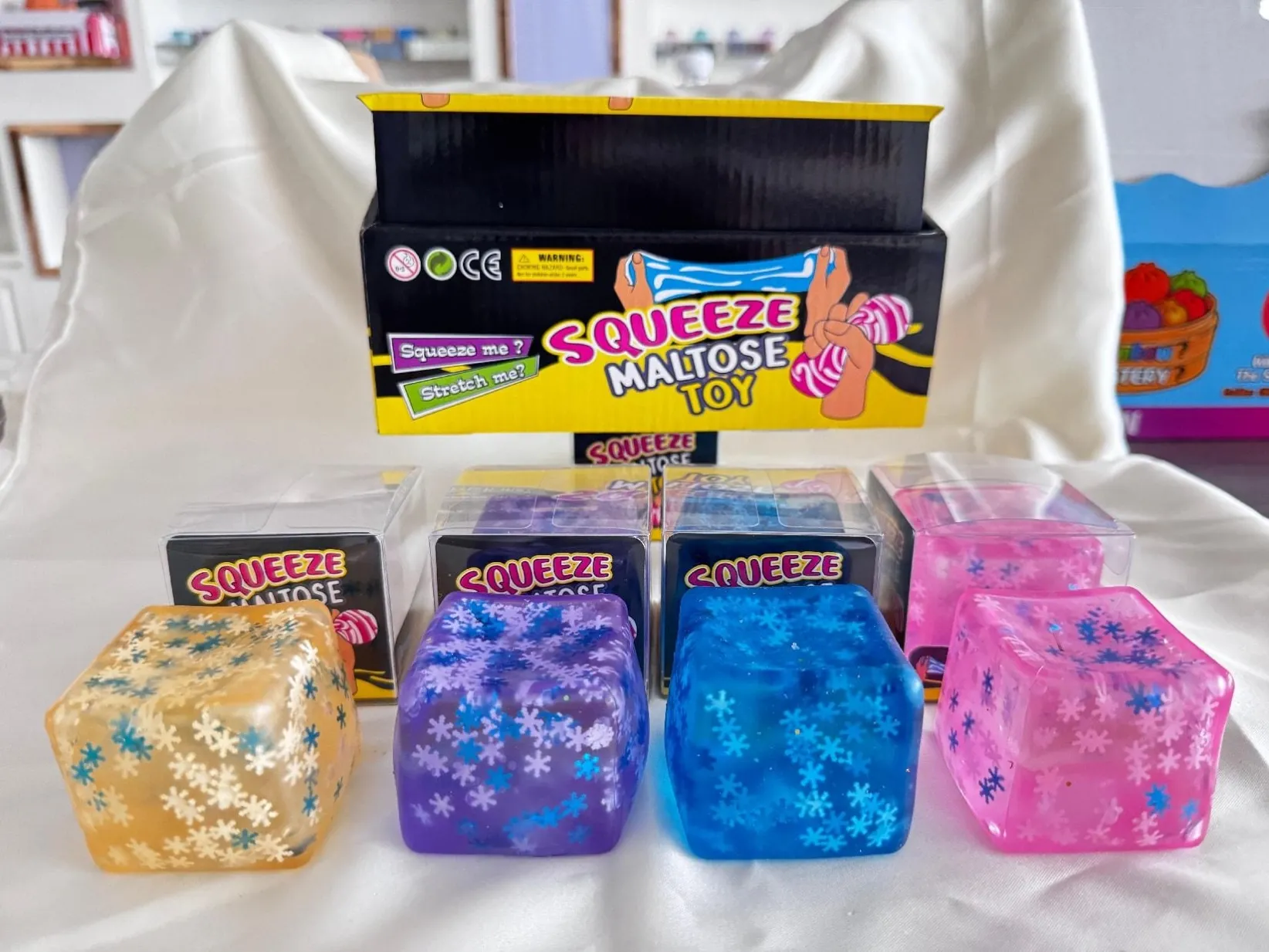 Clear colourful squishy cubes with decorative details in front of a display box