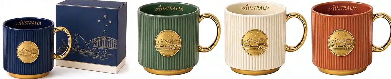 Navy, green, cream and brown ribbed ceramic mugs with Australia emblems and gold-colored handles, shown with a navy gift box.