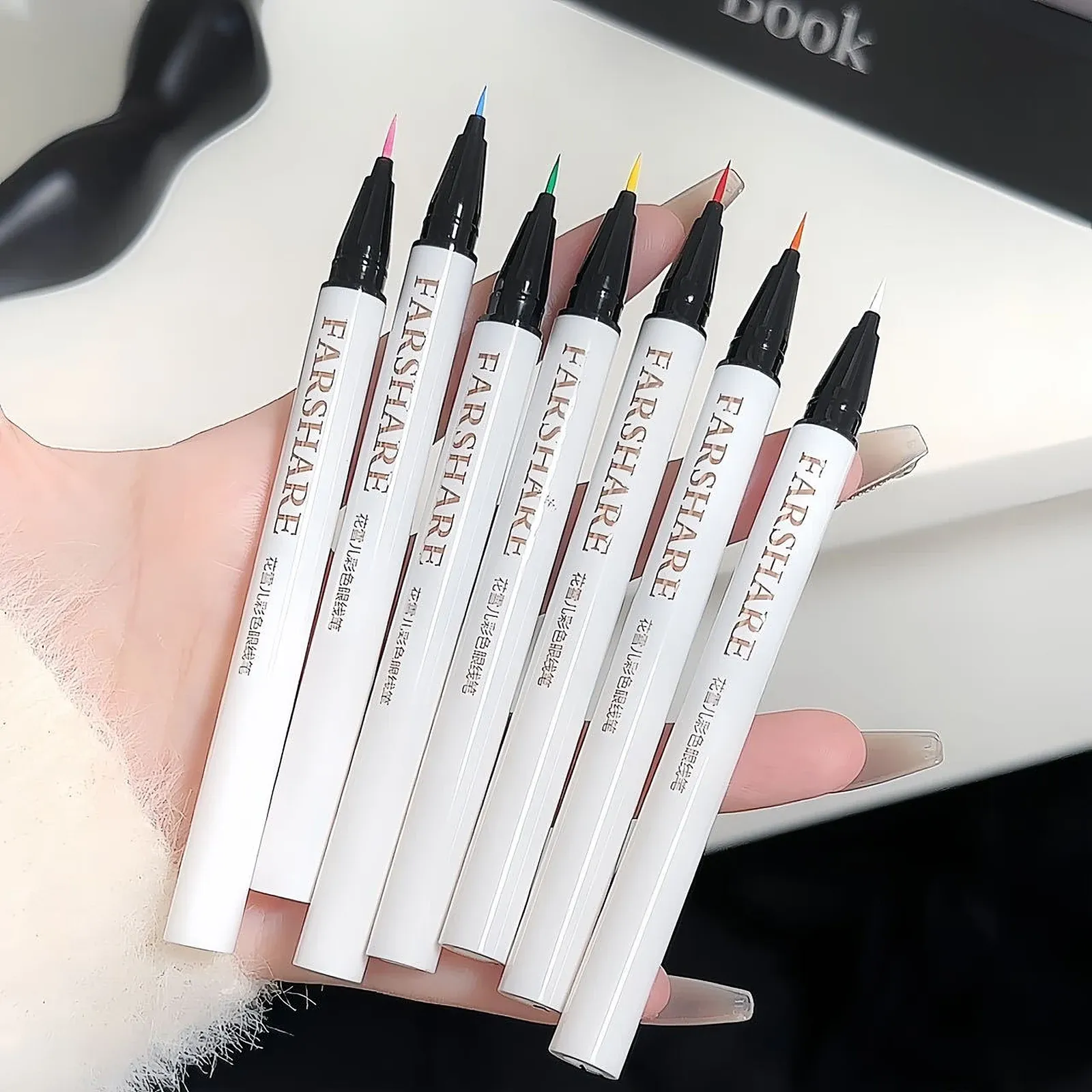 Coloured Liquid Eyeliner Set - Seven slim white eyeliner pens with black caps and fine tips in pink, blue, green, yellow, red, orange and white, each with vertical lettering along the barrel.