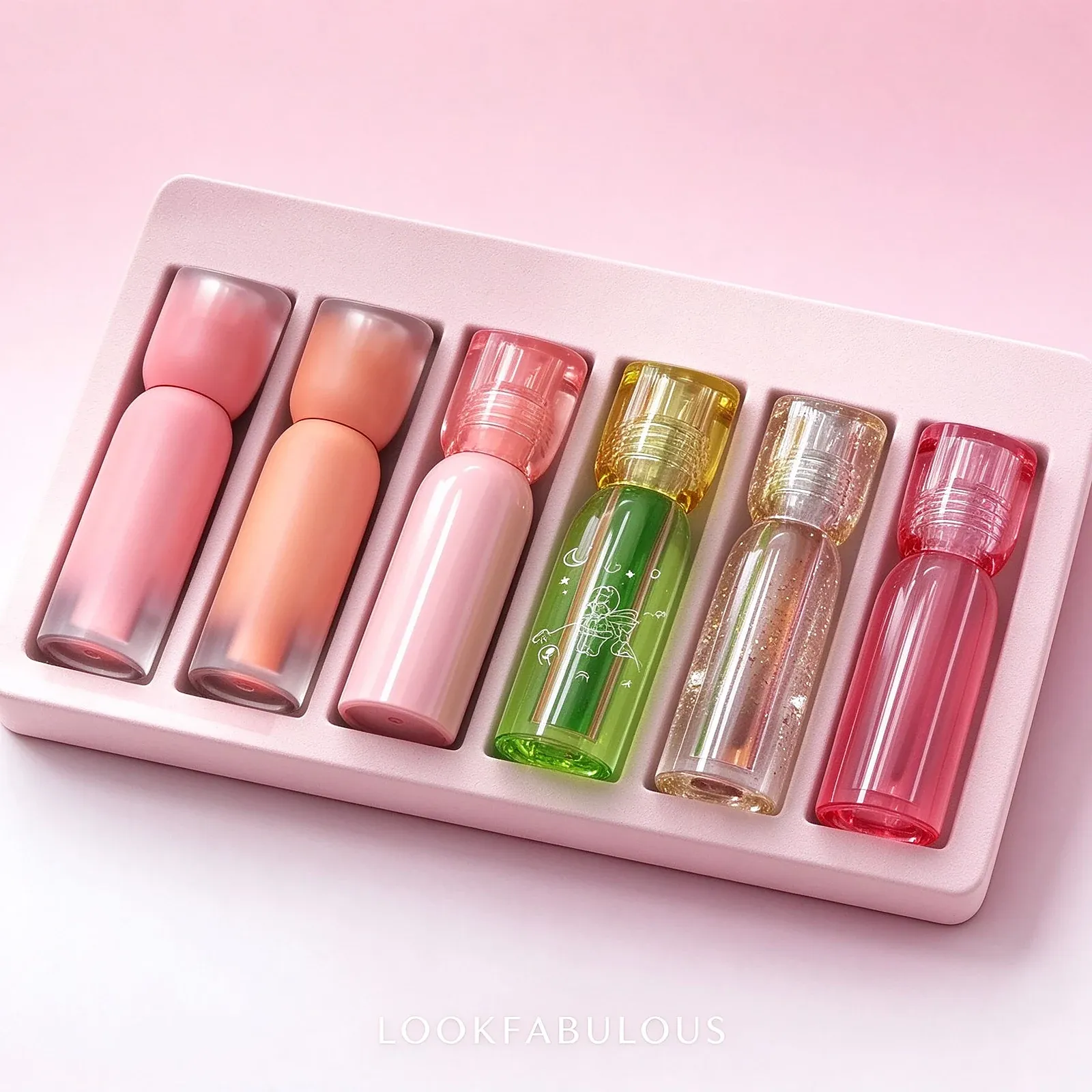 Six mini lip glosses in a pale pink tray, including matte peach and pink tubes, a green illustrated tube, gold shimmer and red gloss