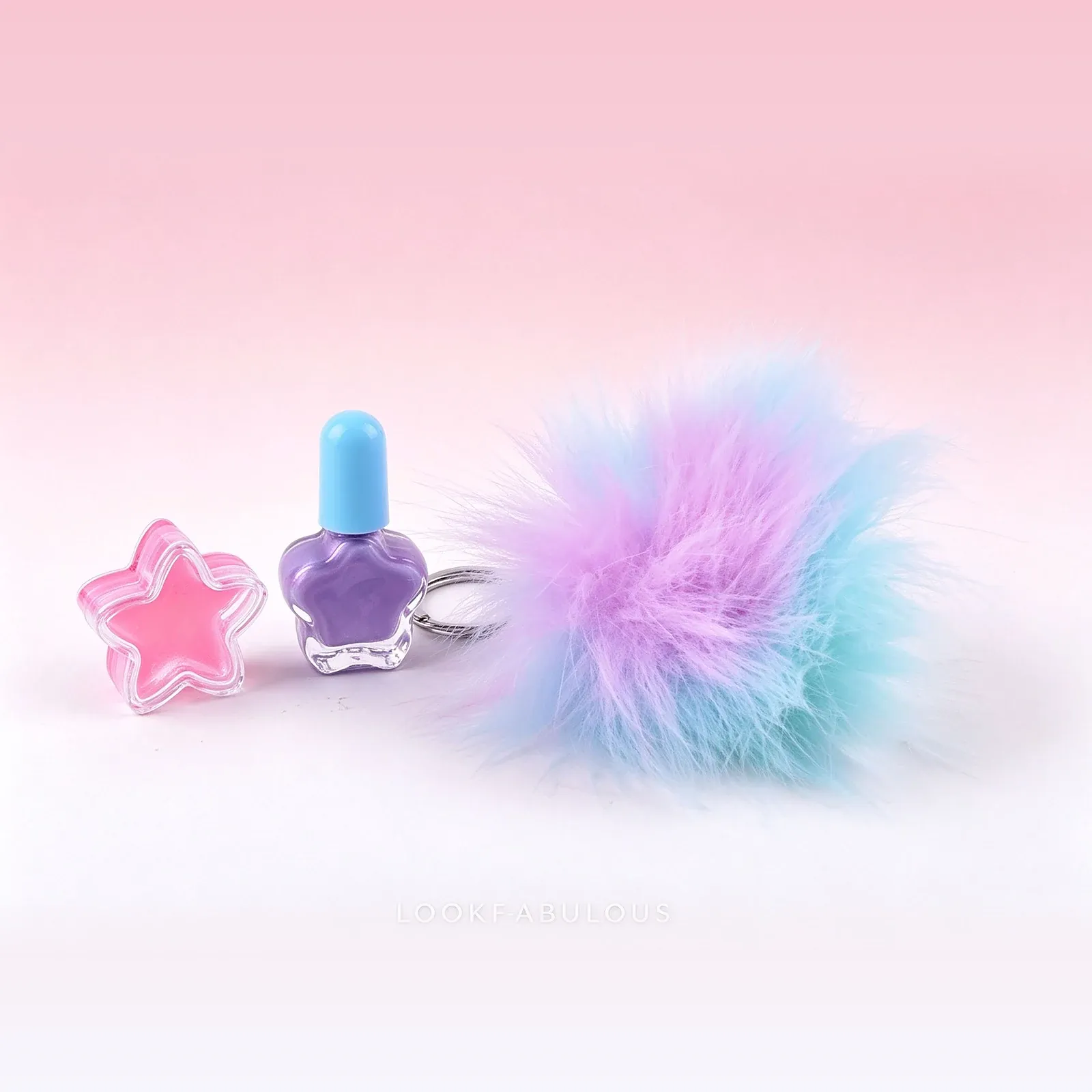 Pink star nail polish, a purple nail polish bottle with a blue cap and a pastel pom-pom keychain