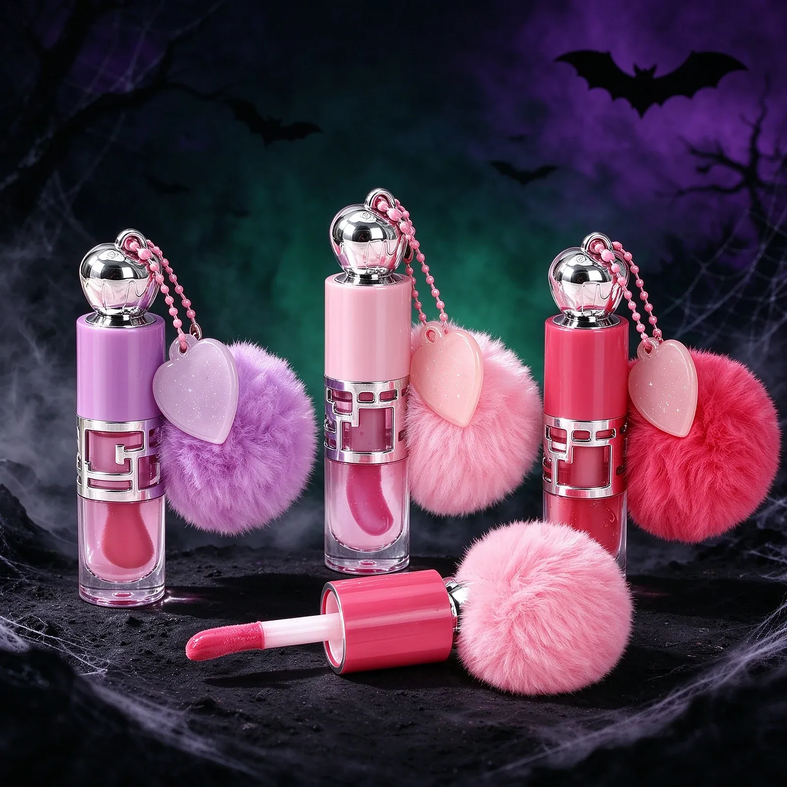 Pom-Pom Heart Charm Lip Gloss Set - Three cylindrical lip glosses with silver ball caps, each on a beaded chain with a translucent heart charm and a fluffy pom-pom in purple, pink and red, one cap removed to show a red doe-foot wand.