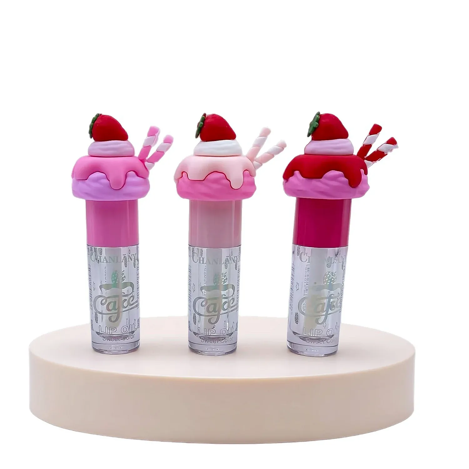 Three silver lip gloss tubes with red Santa hat caps on a small display platform