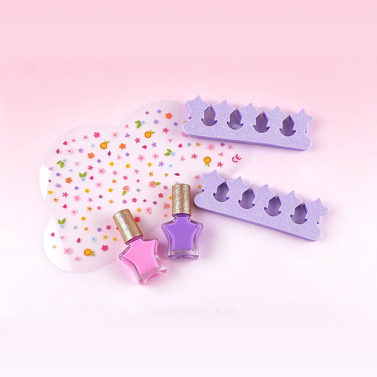 Pink and purple star nail polishes with gold caps beside two glitter press-on nail strips, each with five star-shaped tips, and a flower sticker sheet