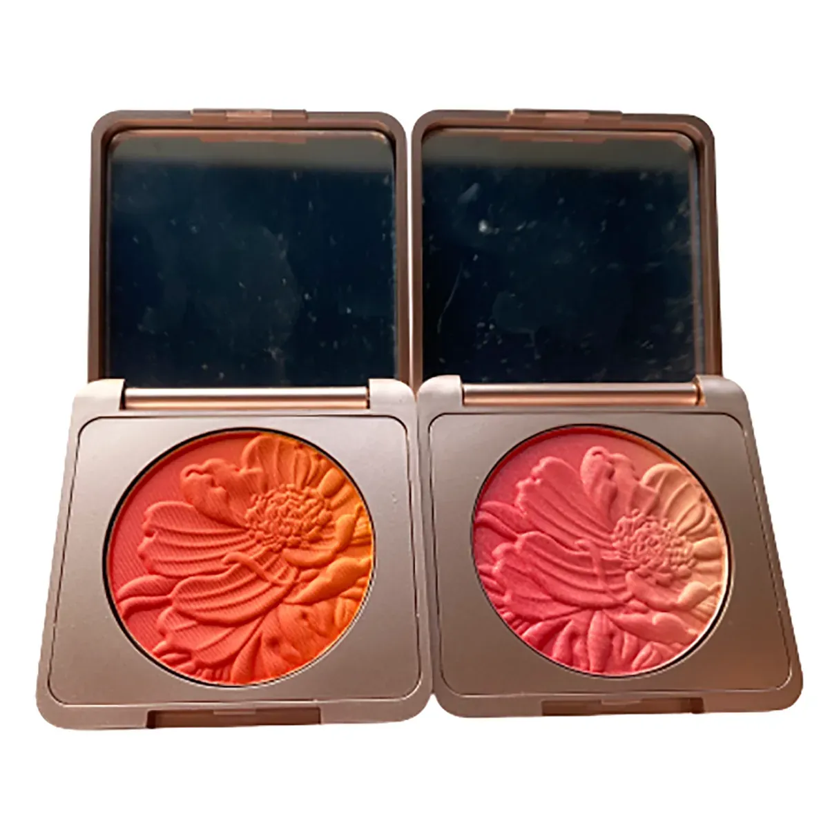 Two flower-embossed blush compacts in coral orange and rose pink with mirrors